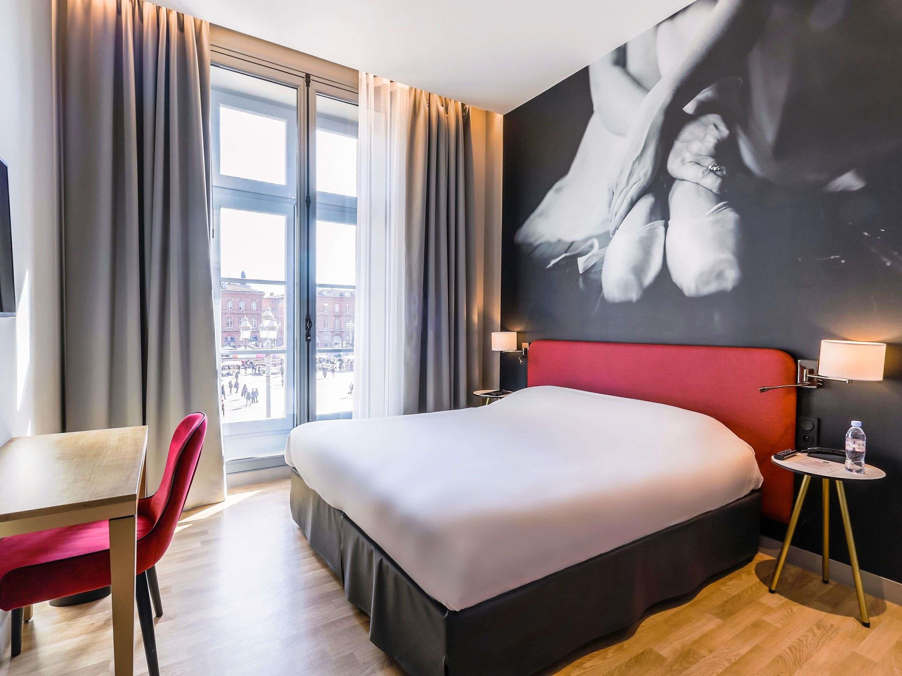 Een hotelkamer met een groot bed, een bureau, een stoel, uitzicht op de stad en een kunstwerk aan de muur.
