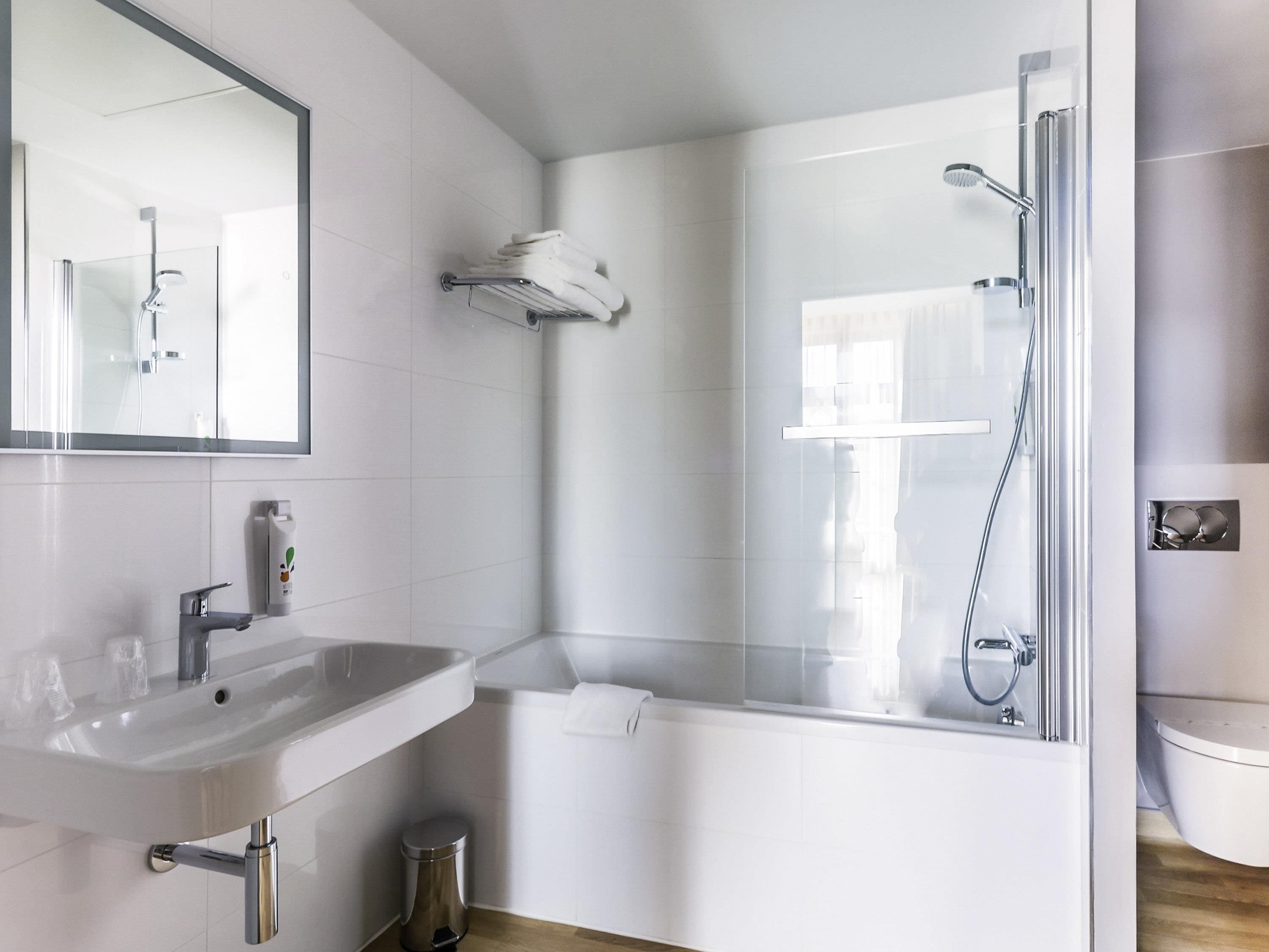 A modern bathroom with a sink, mirror, toilet, and shower.