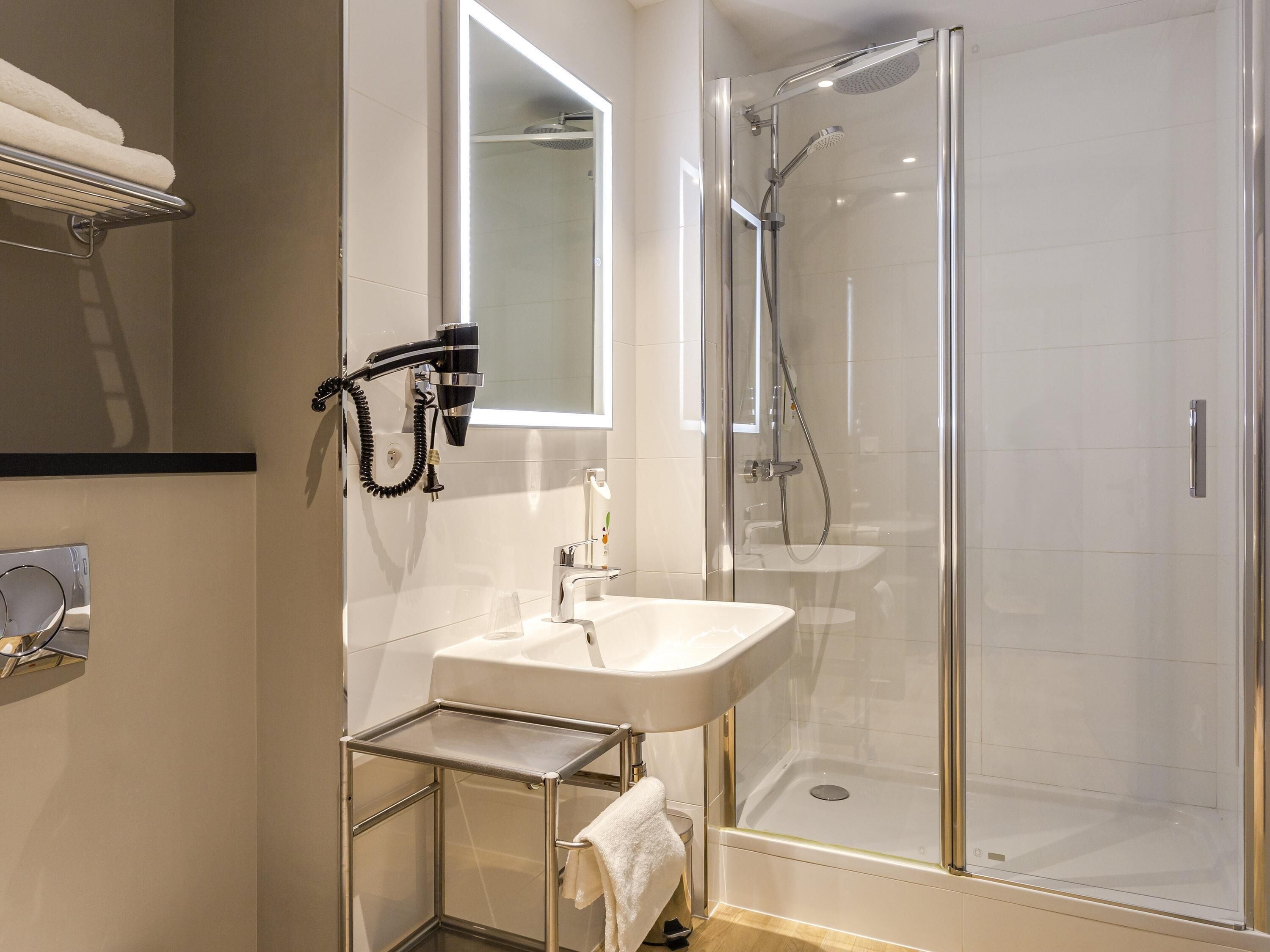 Un baño moderno con ducha envuelta en vidrio, un lavamanos blanco y un perchero para toallas.