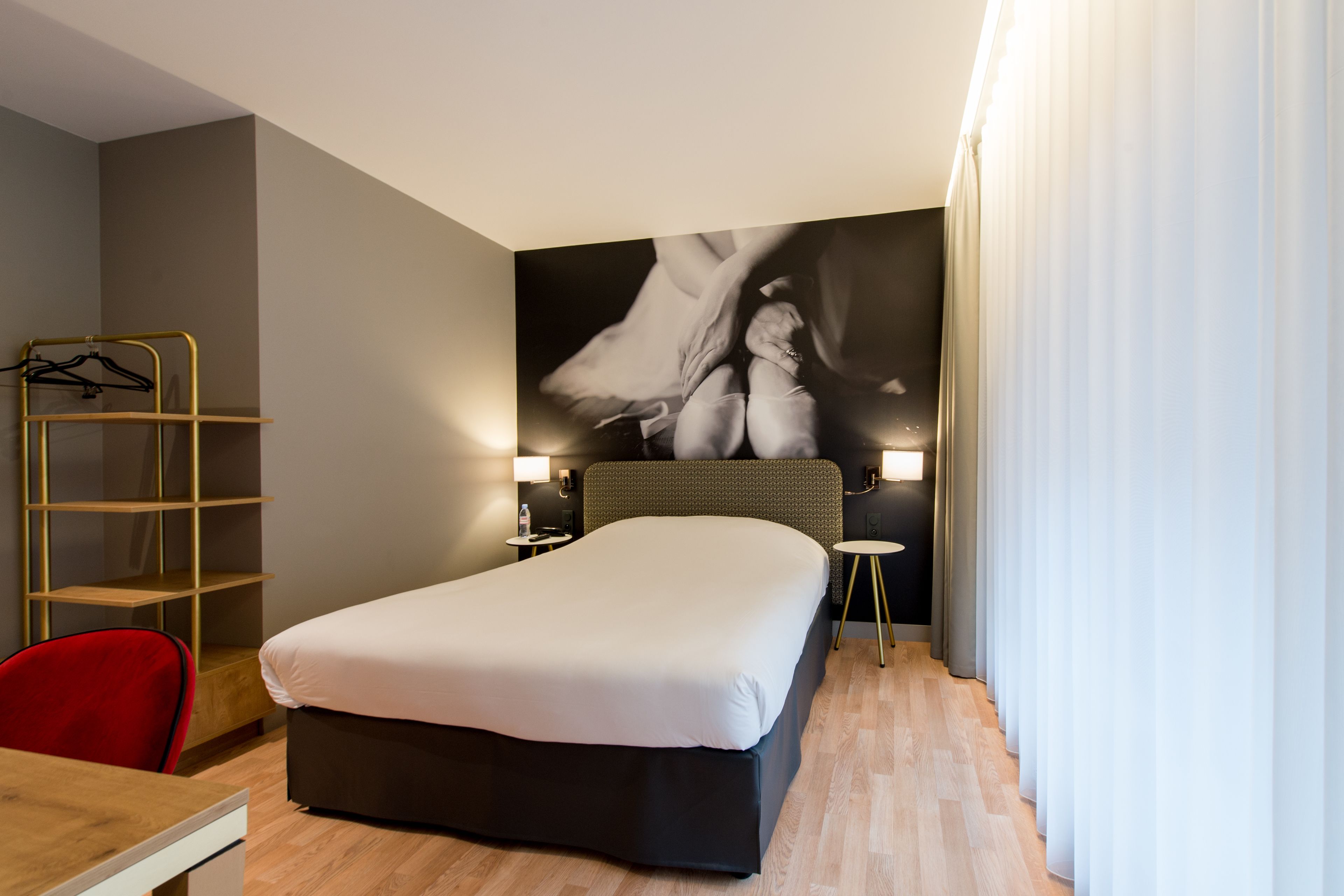 Una habitación de hotel con cama, escritorio, silla, armario y estante en la pared.