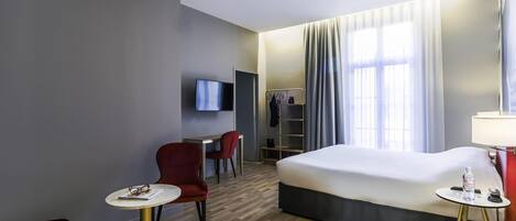 A hotel room with a bed, a desk, two chairs, a TV, and a wardrobe.