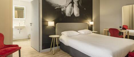 Une chambre d’hôtel avec un grand lit, une table de chevet, une chaise rouge, une petite table ronde et un miroir fixé au mur.