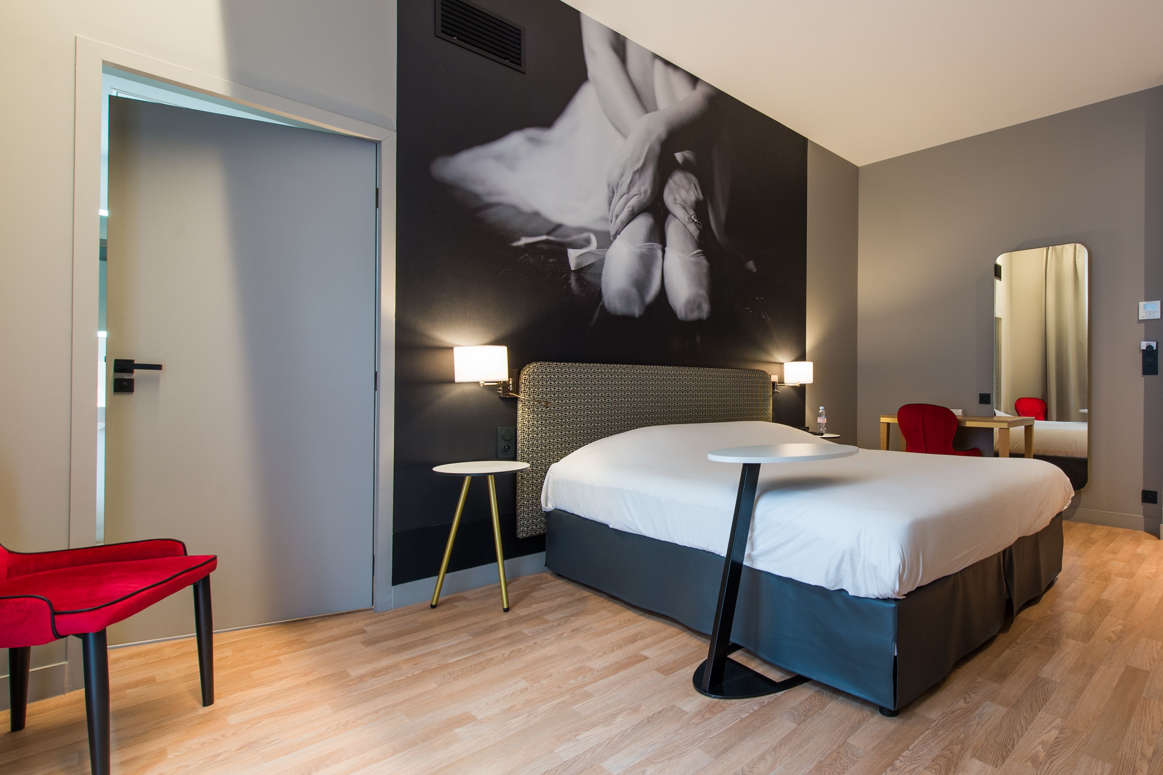 Ein modernes Hotelzimmer mit einem großen Bett, einem roten Sessel, einem kleinen Tisch und einem wandmontierten Spiegel.