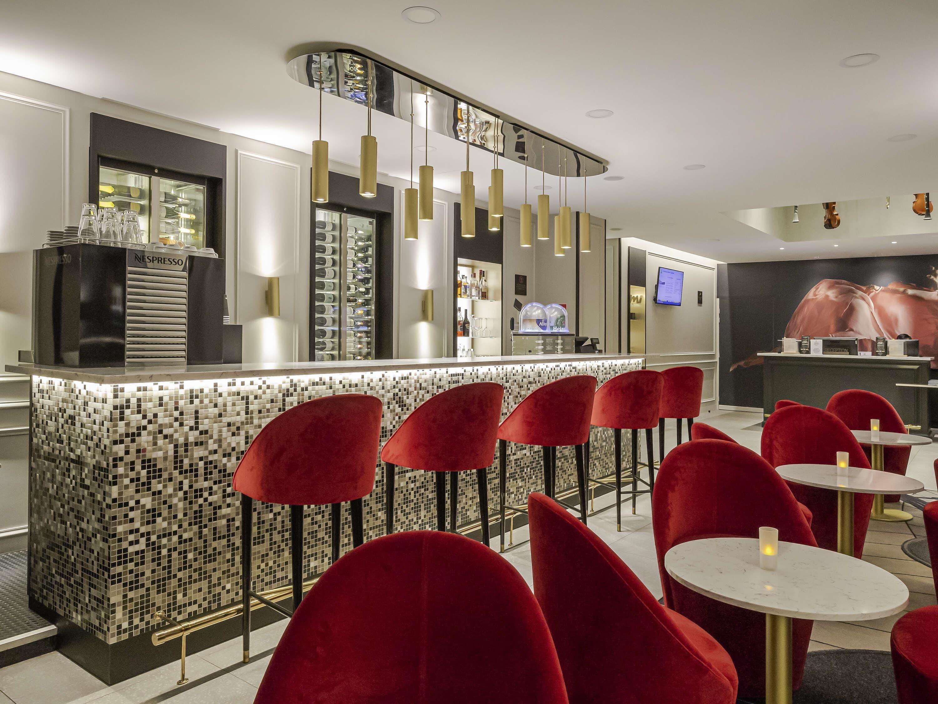 Eine moderne Bar mit einer Mosaik-Fliesen-Theke, roten Samtstühlen und Pendelleuchten.