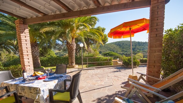 Un patio al aire libre con una mesa lista para comer, sillas y un área de descanso con una sombrilla de playa.