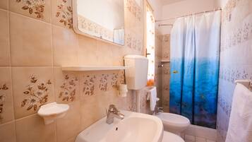 Une salle de bain avec un lavabo, deux toilettes, un miroir et un rideau de douche orné de motifs de poissons.