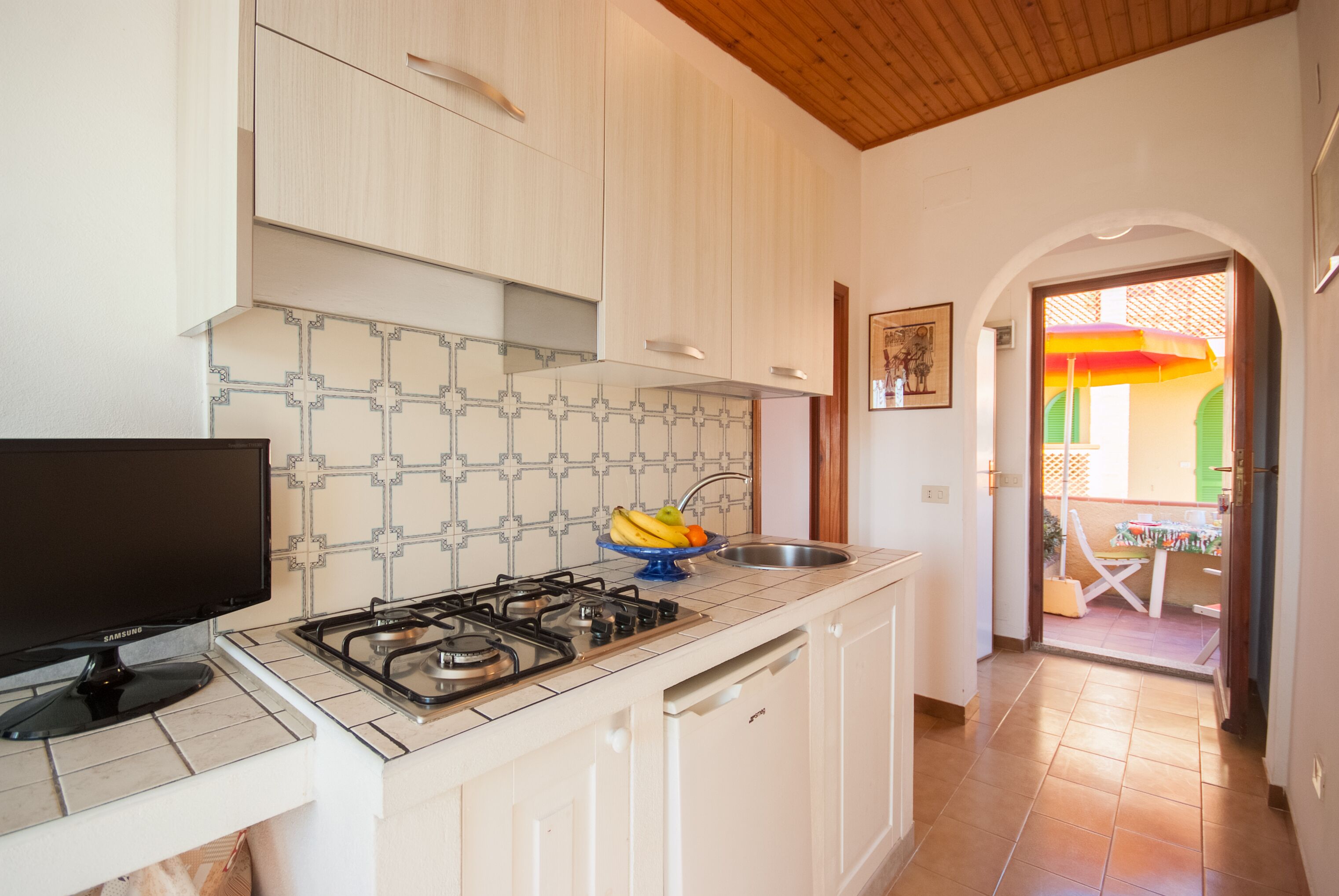 Une cuisine avec des meubles blancs, une cuisinière à gaz, un évier et un téléviseur Samsung.