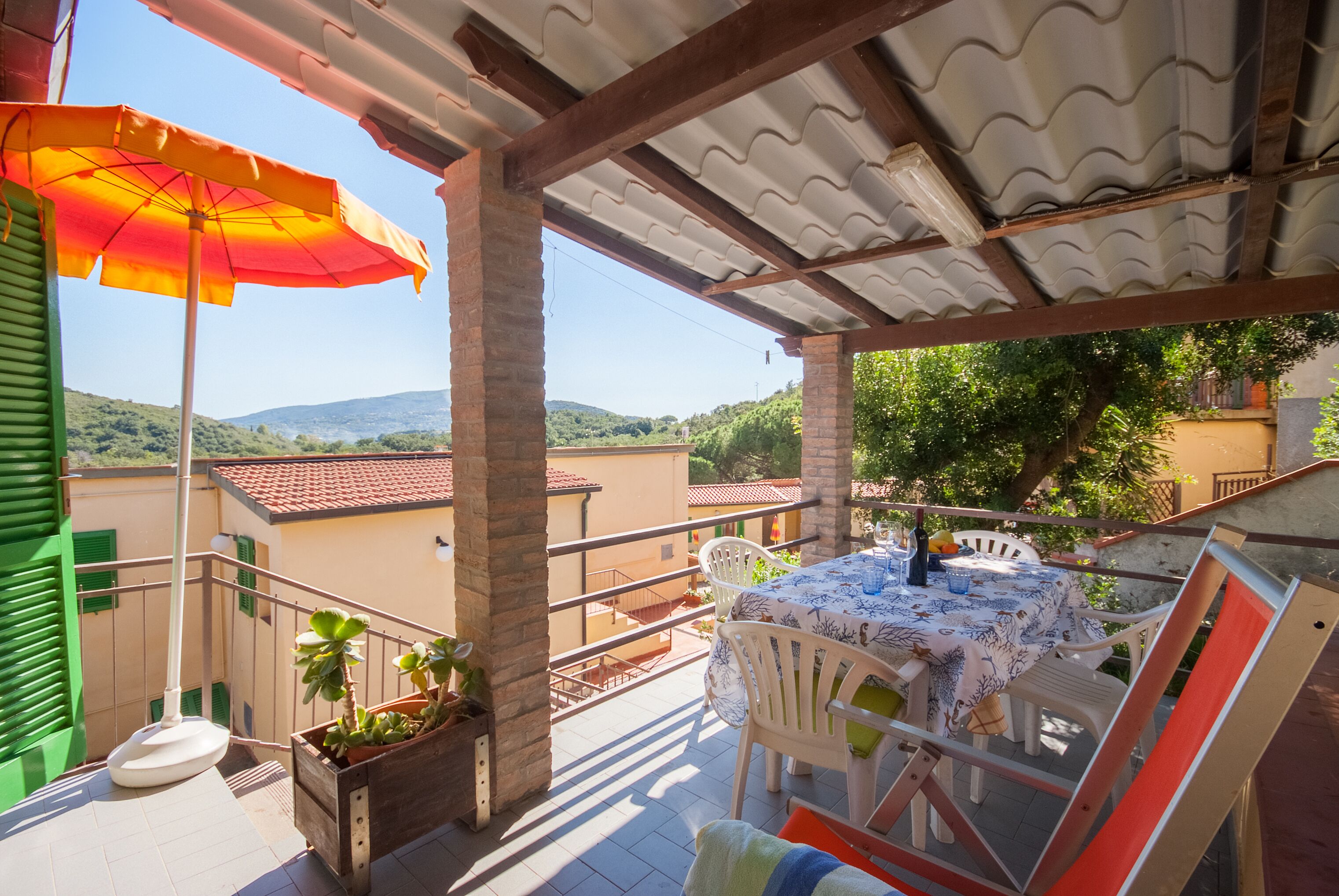 Un balcon avec une table dressée pour deux personnes, une plante en pot et un grand parasol.
