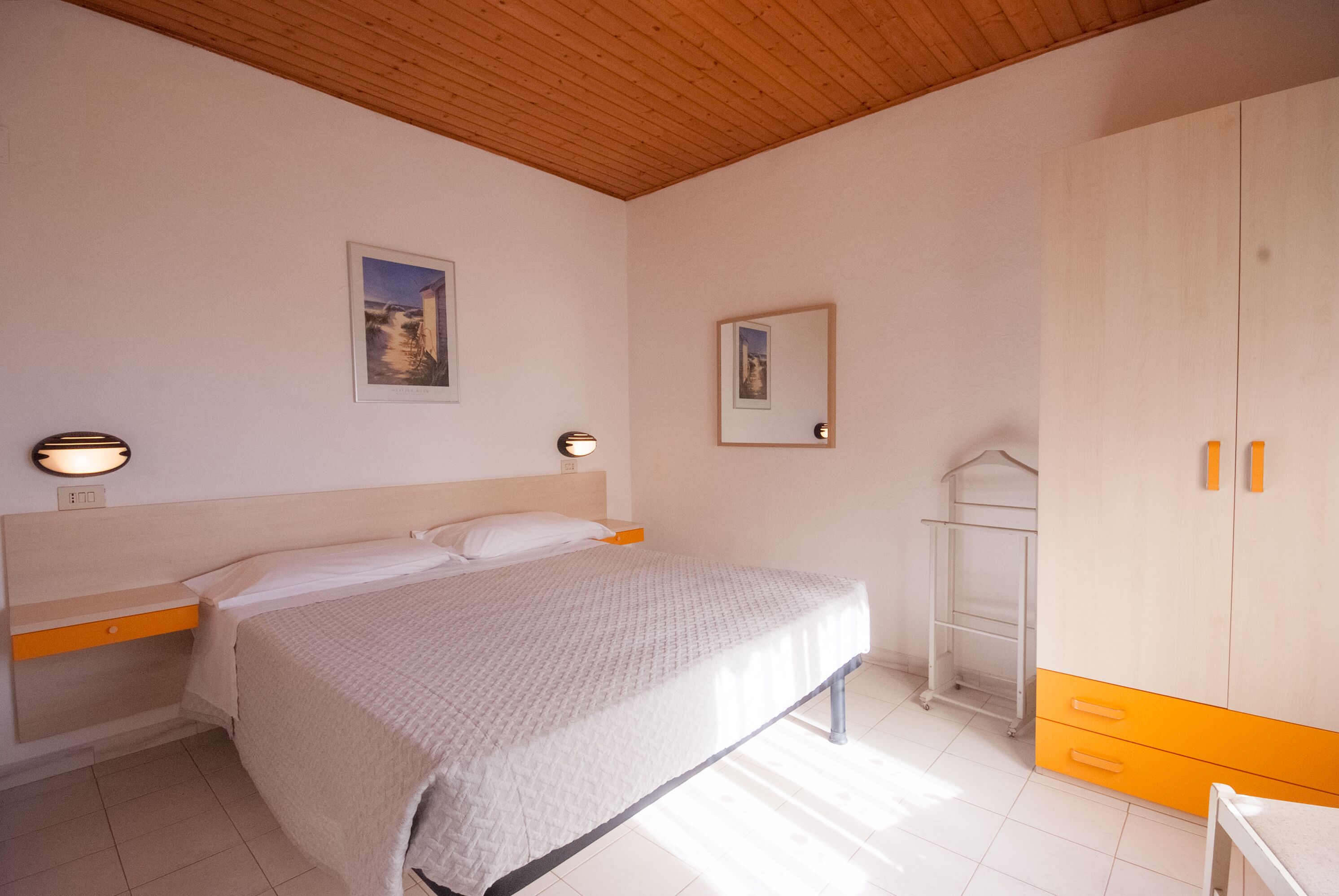 A bedroom with a bed, bedside table, wardrobe, and wall-mounted light fixtures.