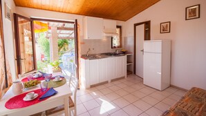 Una cocina con armarios blancos, un refrigerador blanco y una zona de comedor con una mesa para dos.