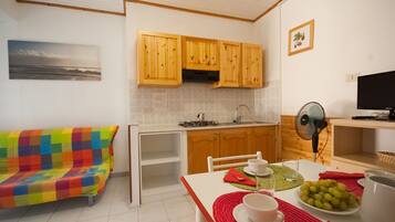 A compact kitchen with wooden cabinets, a dining table with a red placemat, and a colorful sofa.