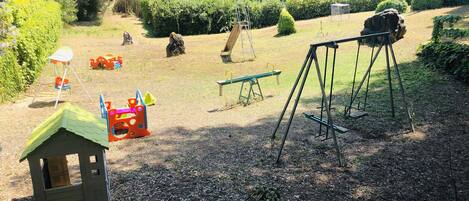 Une aire de jeux avec des balançoires, une bascule et une petite maison de jeu.