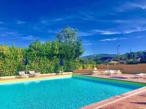 A clear blue swimming pool with lounge chairs and umbrellas, surrounded by lush greenery and a view of hills in the background. - Residence La Valdana (Capoliveri)
