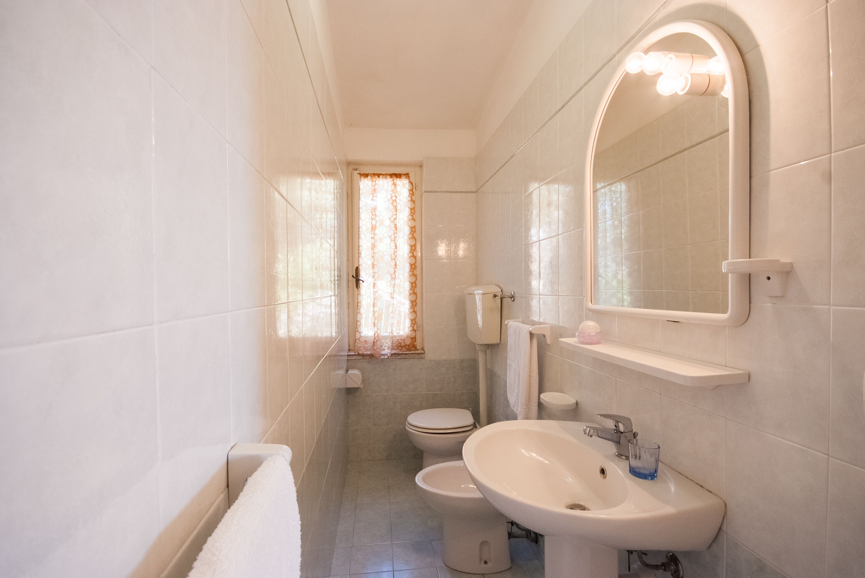 Ein Badezimmer mit Toilette, Bidet, Waschbecken und einem beleuchteten Spiegel.