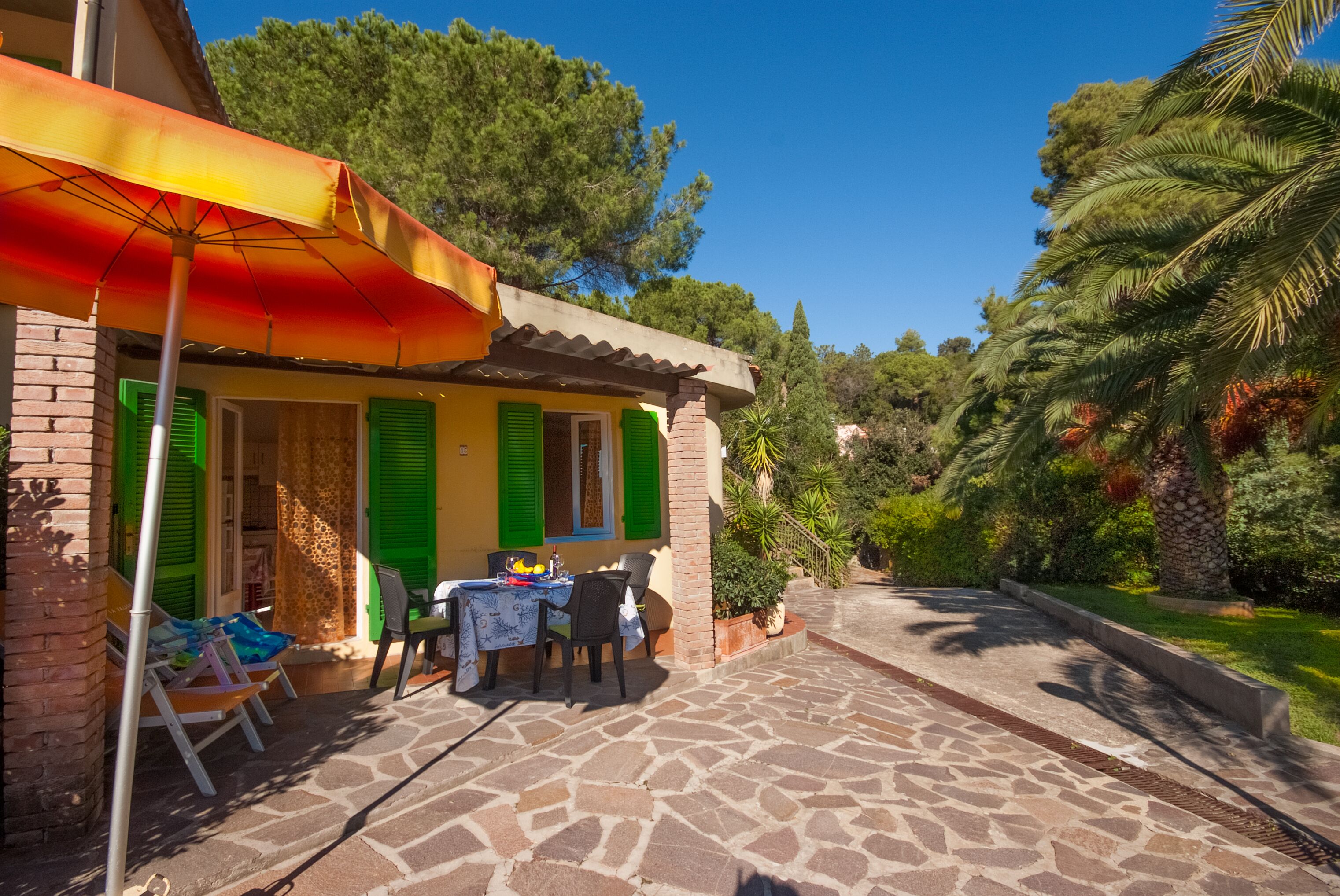 A patio with a table and chairs, a brick wall, and a colorful umbrella.
