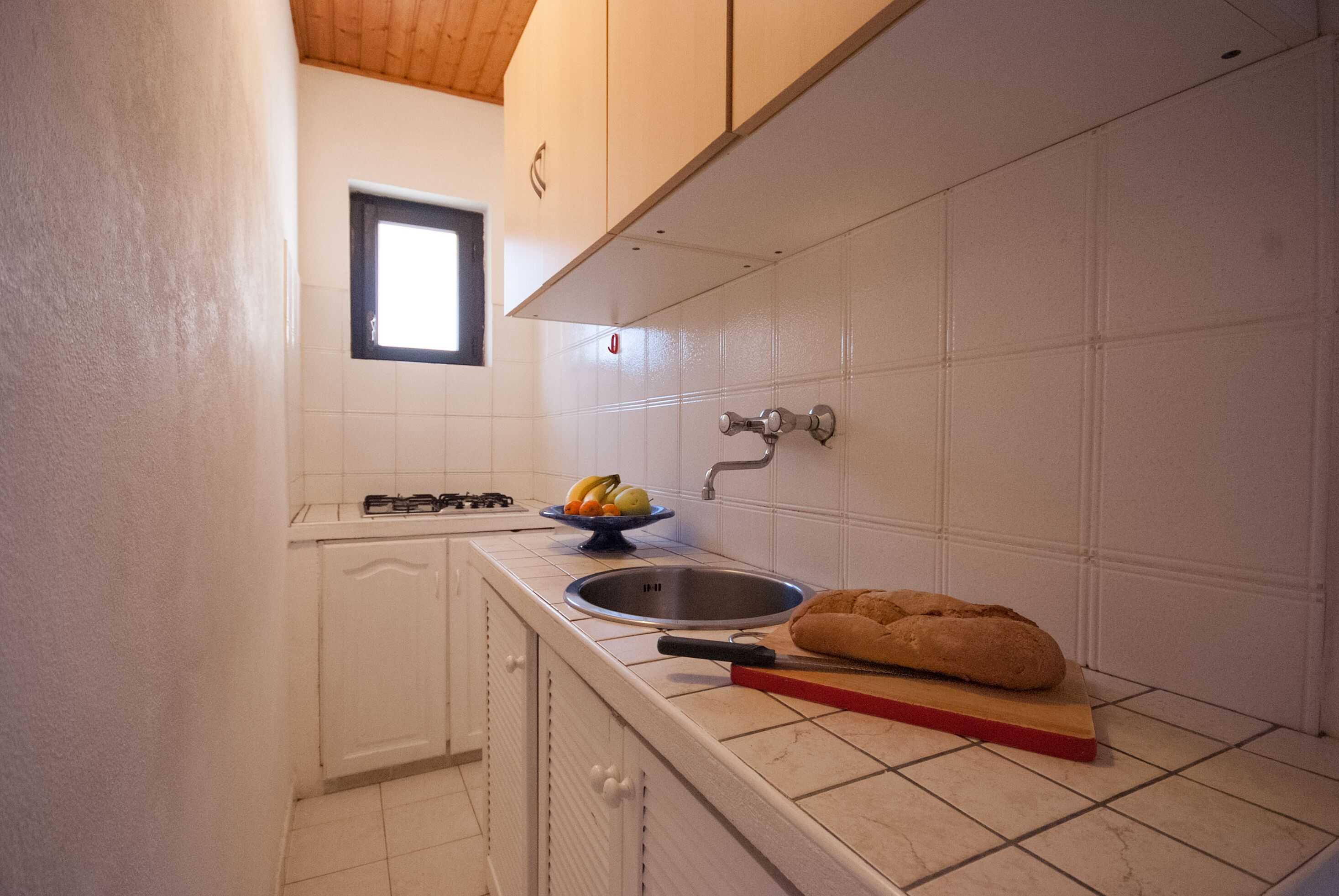 A kitchen with white cabinets, a window, a sink, a gas stove, and a loaf of bread on the counter.