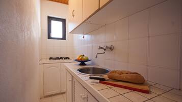 A kitchen with white cabinets, a window, a sink, a gas stove, and a loaf of bread on the counter.