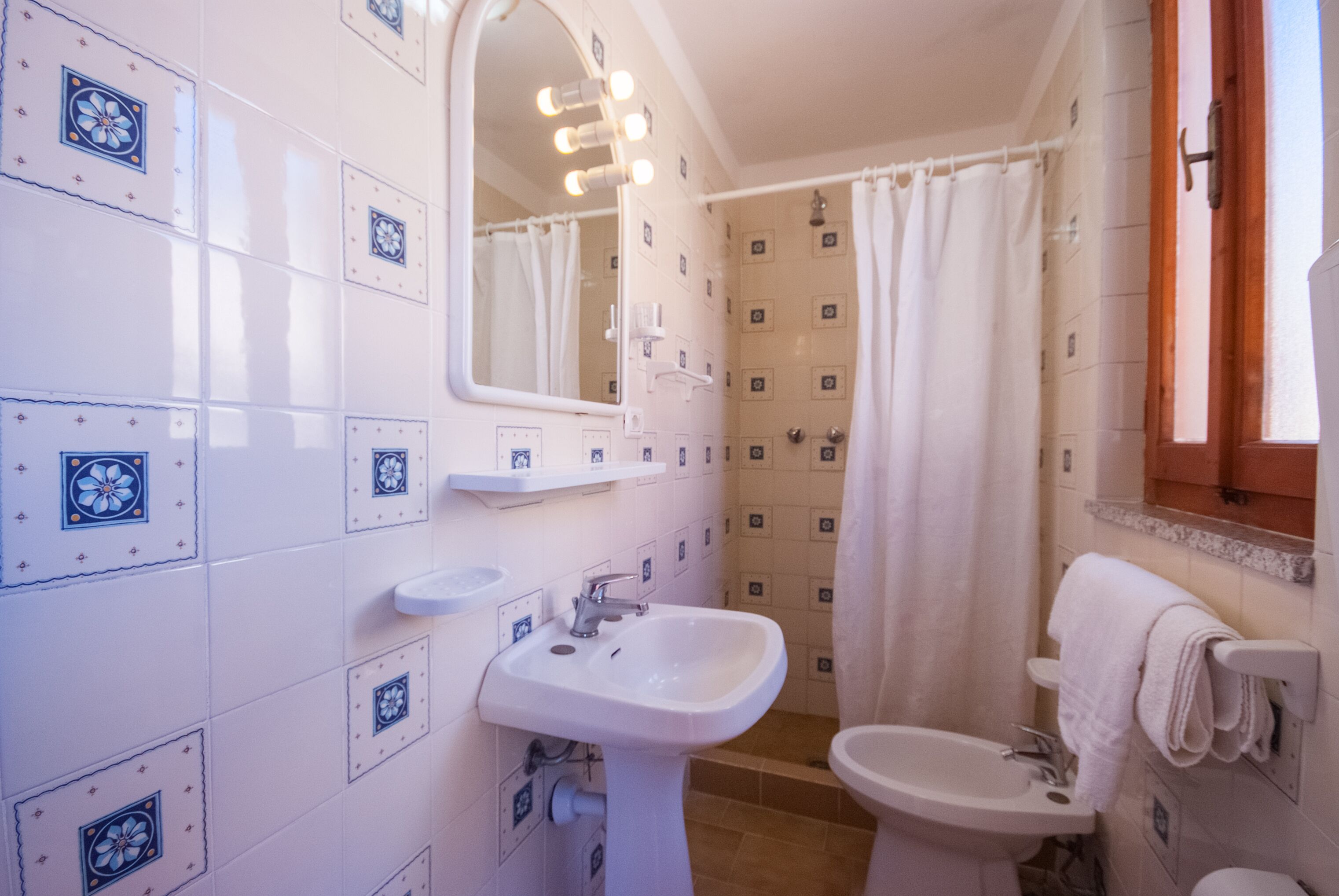 Un baño con azulejos blancos, un lavamanos, un espejo y una cortina de ducha.