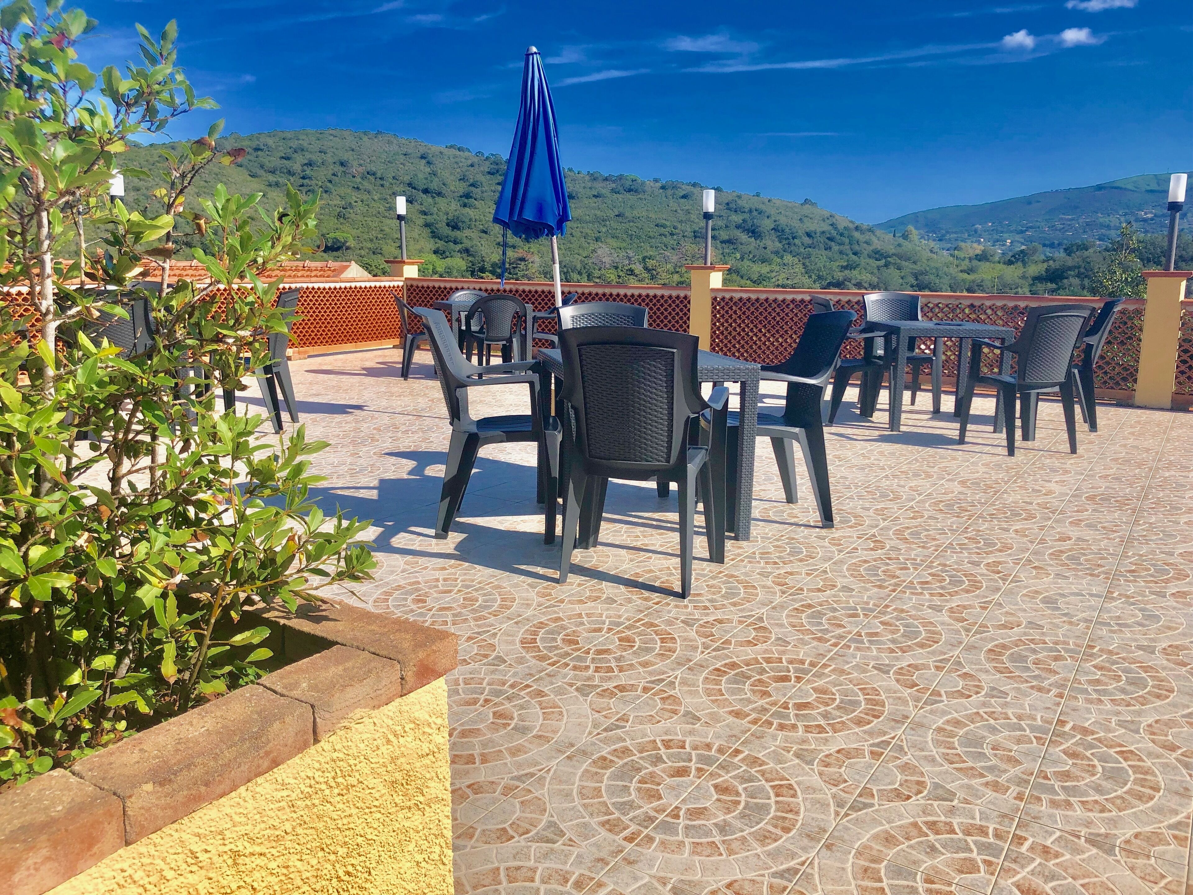 An outdoor patio with tiled flooring, black wicker chairs, and a blue umbrella.