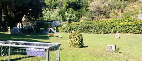 A fenced soccer field with a goalpost, a swing set, and a hedge.
