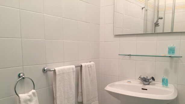 A bathroom with white tiles, a sink, a mirror, and two towels hanging on a towel rack. - Hotel Castelsardo Domus Beach (Castelsardo)