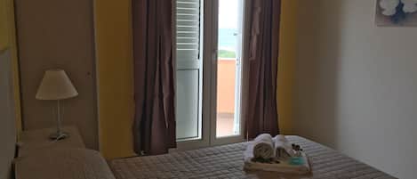Ein Hotelzimmer mit einem Bett, einem Nachttisch mit Lampe, einem Fenster mit Vorhängen und Blick nach draußen.