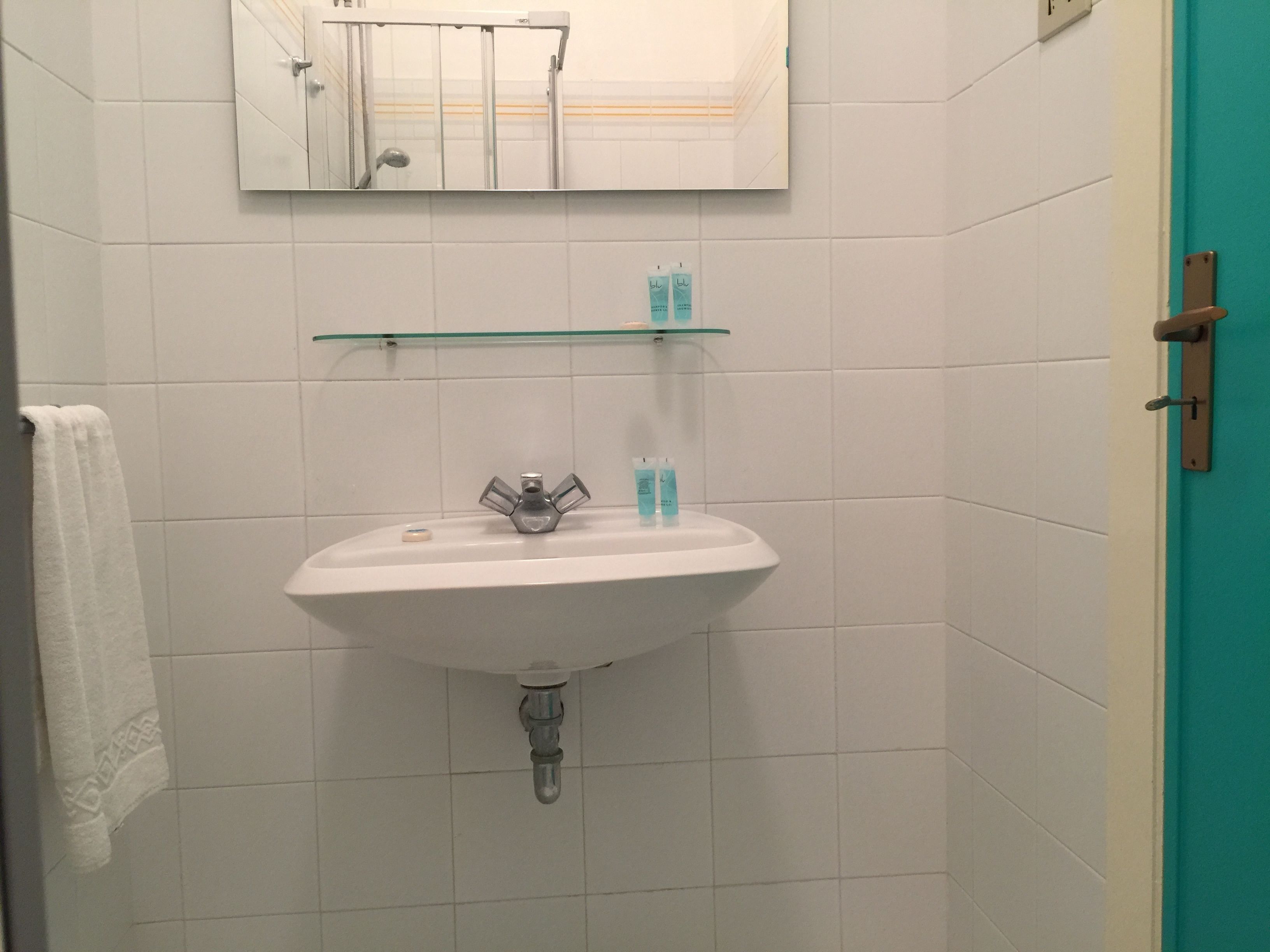 A bathroom with a white sink, a mirror above it, and a glass shelf with toiletries.