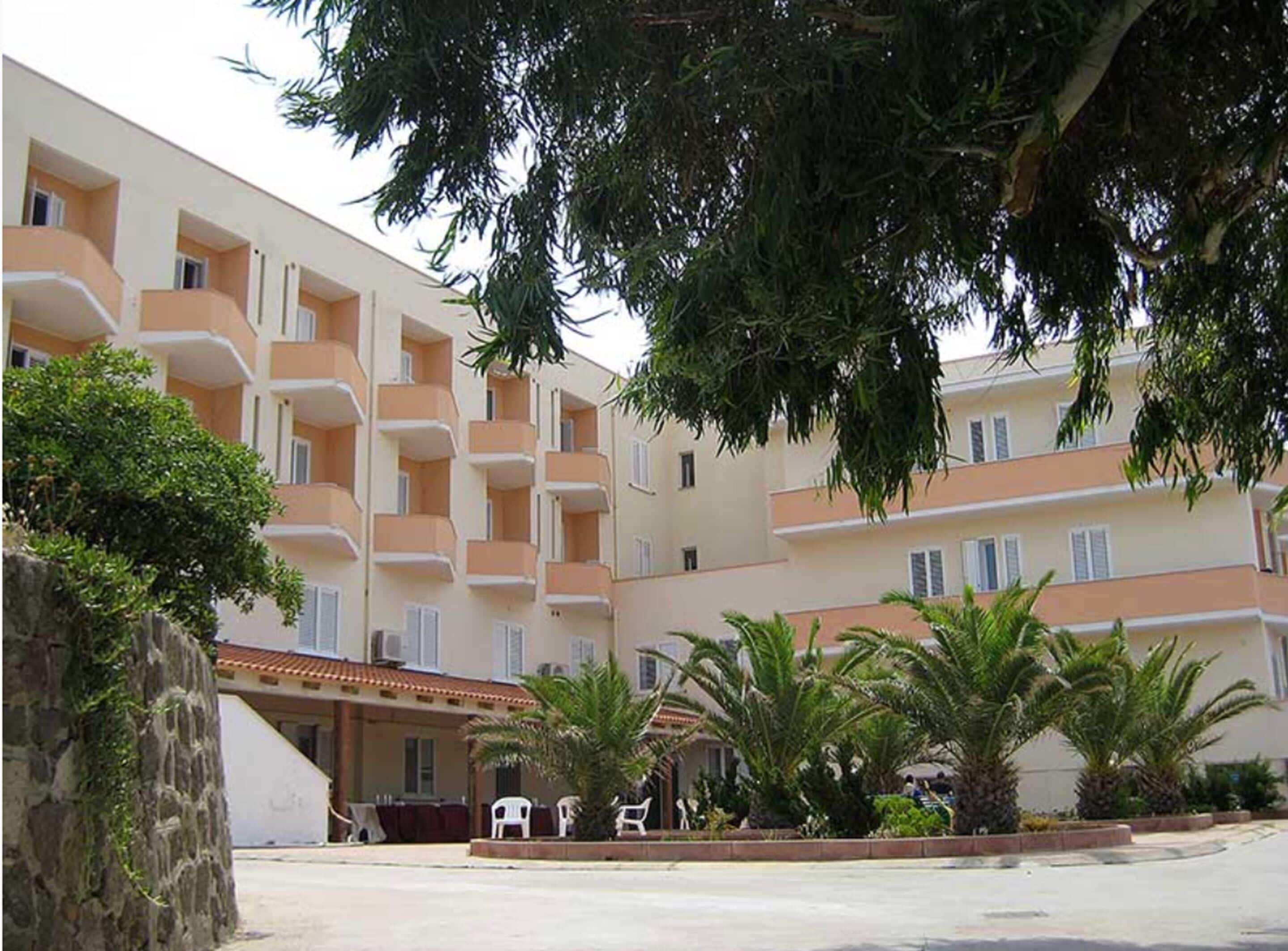 A multi-story hotel with balconies, palm trees, and a stone wall.
