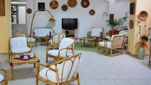 A spacious room with wicker furniture, a flat-screen TV, and decorative plates on the wall. - Hotel Castelsardo Domus Beach (Castelsardo)