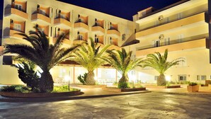 A multi-story hotel with balconies, palm trees, and a well-lit courtyard. - Hotel Castelsardo Domus Beach (Castelsardo)