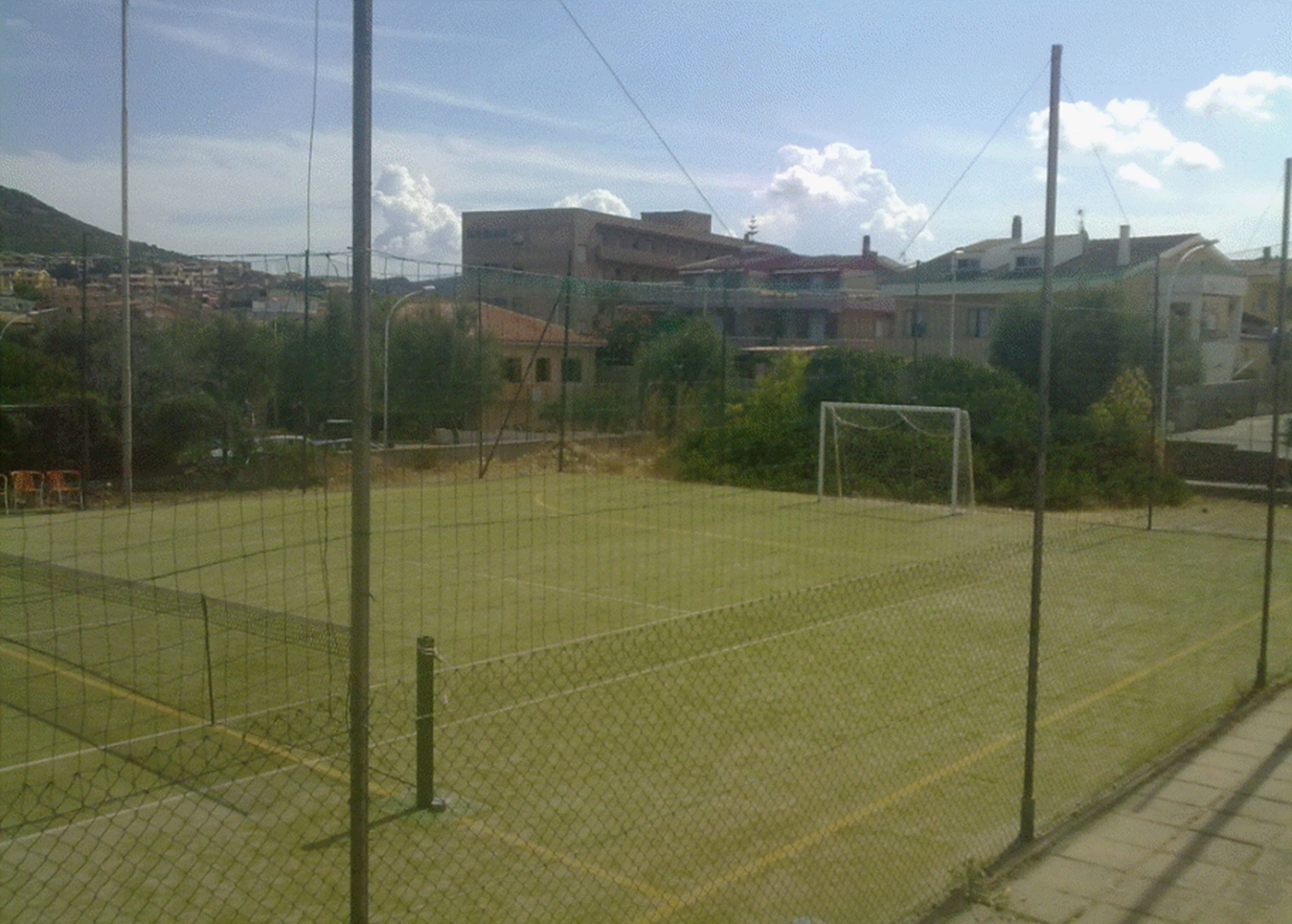 A fenced sports field with a goalpost, surrounded by buildings and trees.