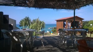 An outdoor seating area with plastic chairs and tables, overlooking a beach and the ocean. - Hotel Castelsardo Domus Beach (Castelsardo)