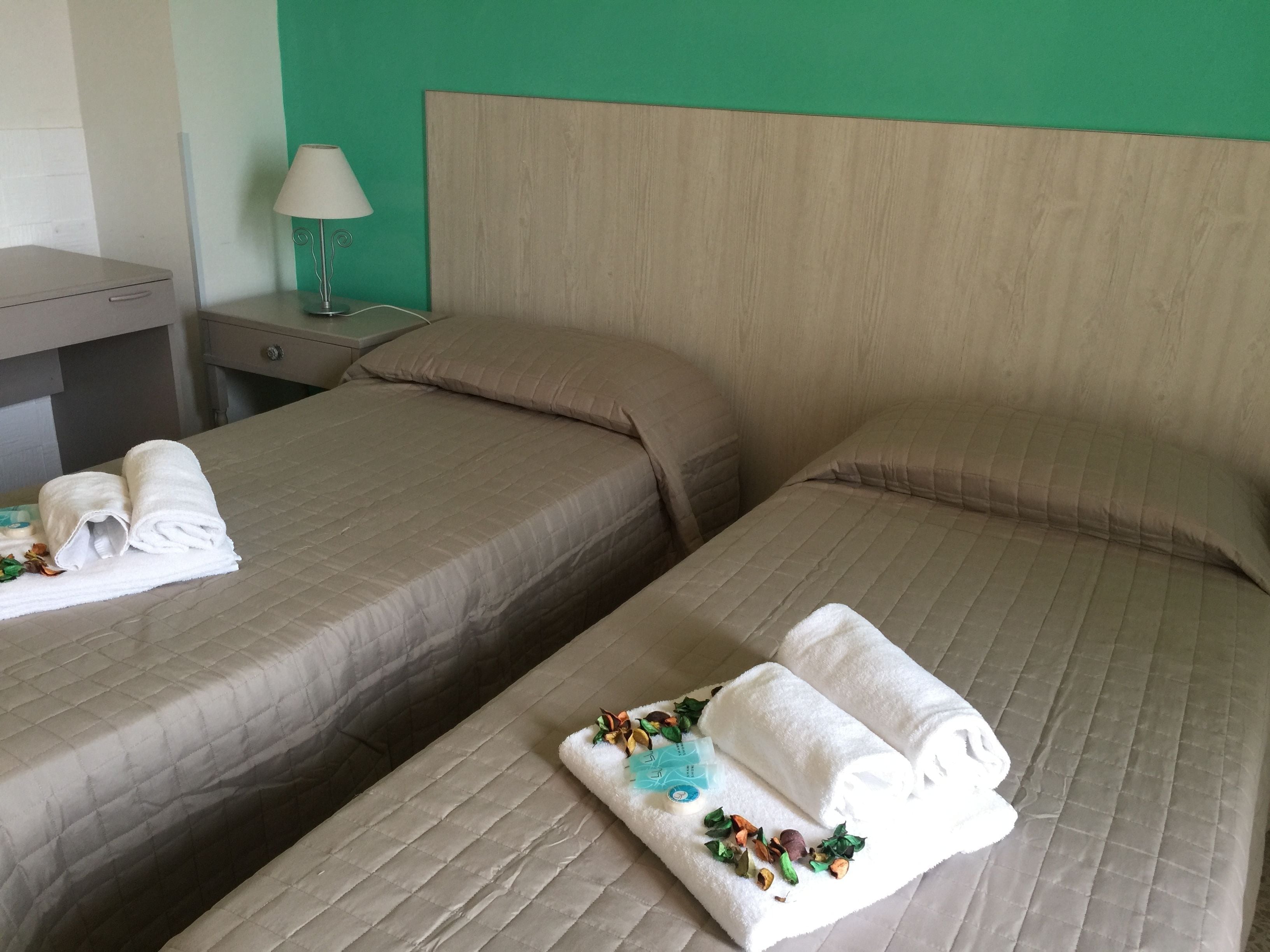 Dos camas individuales con ropa de cama color beige, una mesita de noche con lámpara y una pared verde.