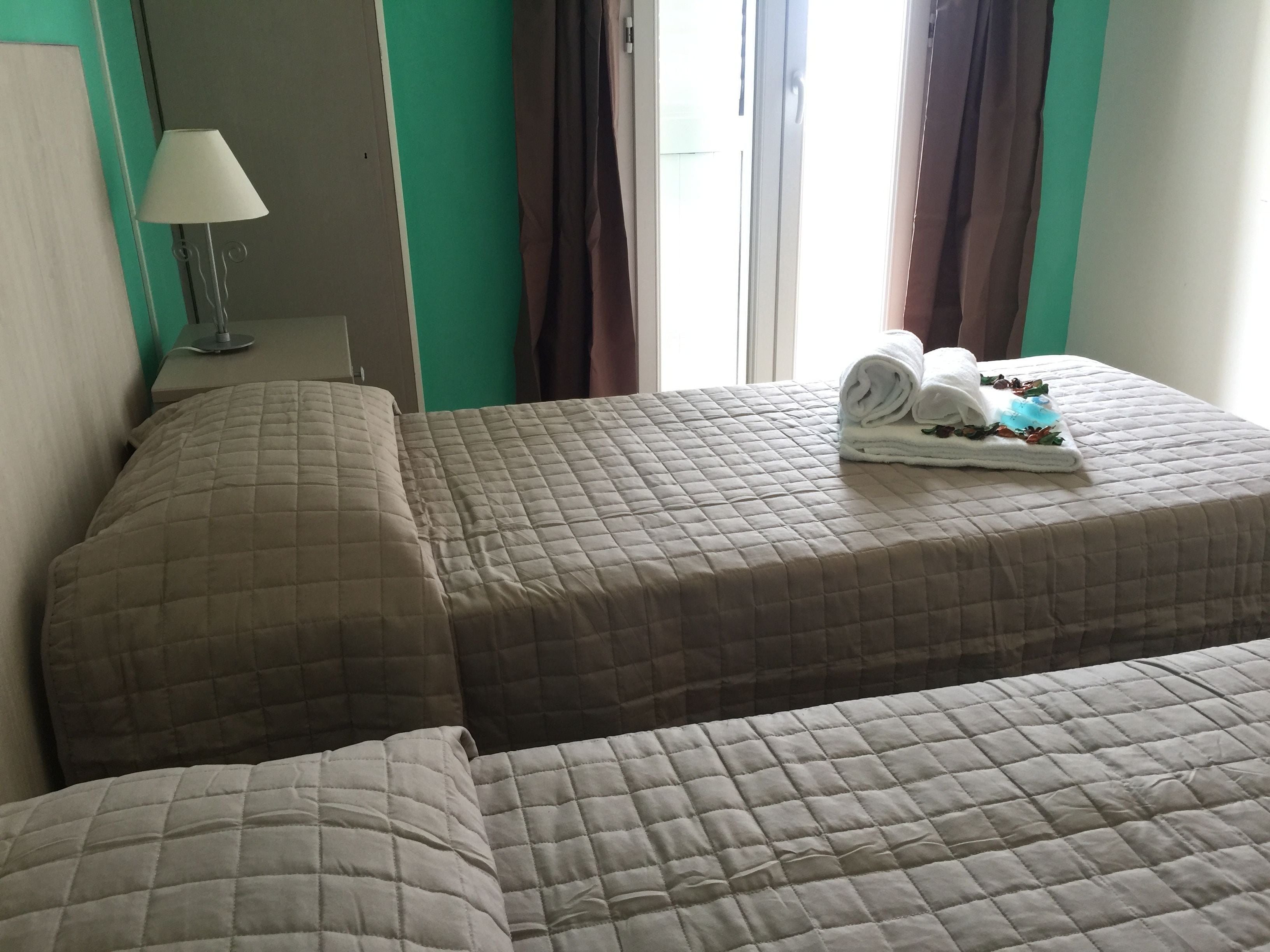 A hotel room with two beds, a lamp, and a window with curtains.