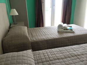 A hotel room with two beds, a lamp, and a window with curtains. - Hotel Castelsardo Domus Beach (Castelsardo)