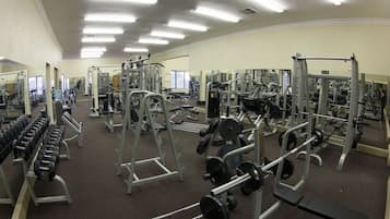 Academia com diversos equipamentos de musculação, espelhos e piso coberto de carpete.