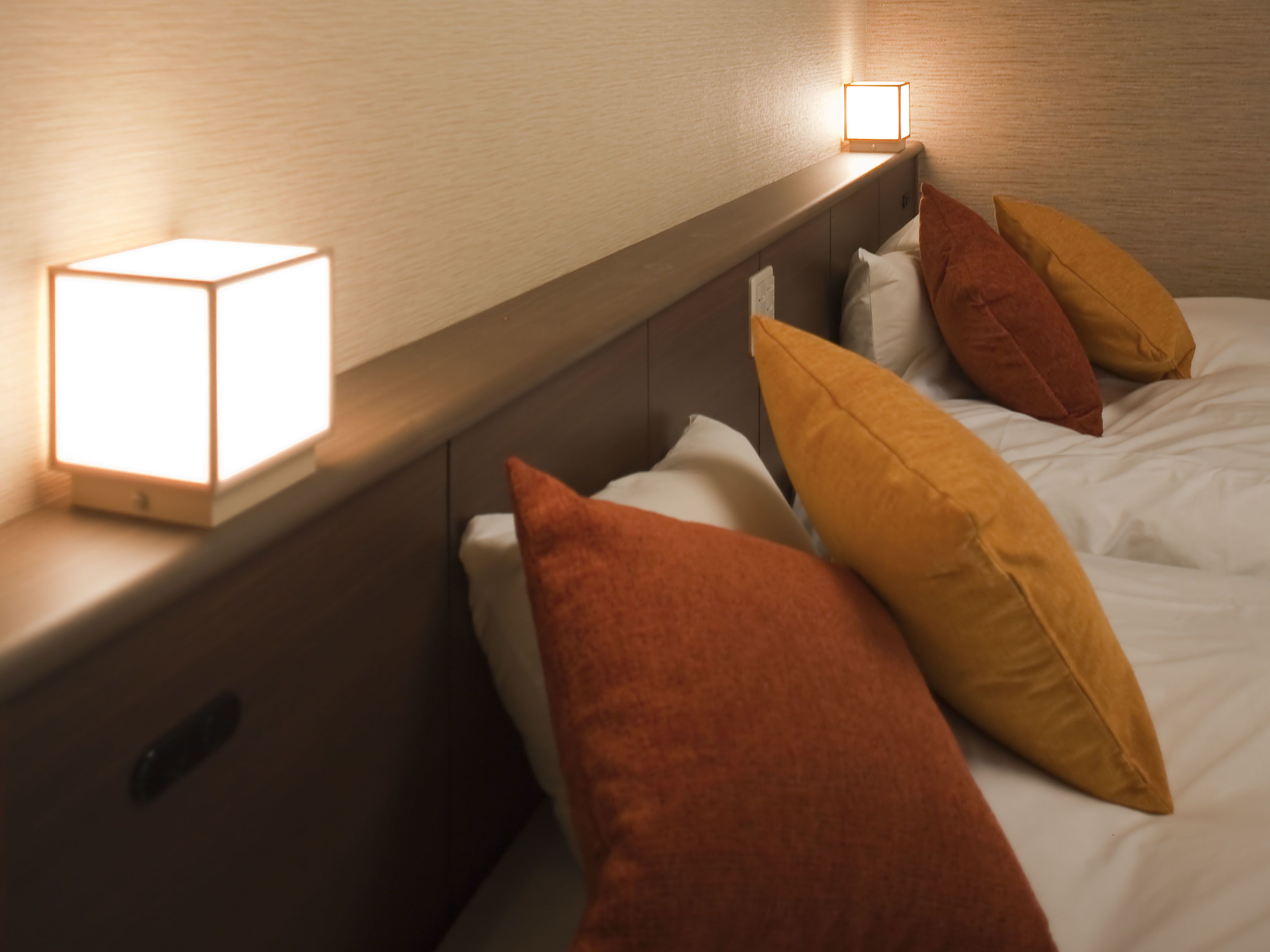 A neatly made bed with multiple pillows, a bedside lamp, and a wooden headboard.