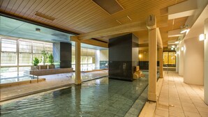 Una piscina interior con agua cristalina, vigas de madera en el techo y amplios ventanales que dejan entrar luz natural.
