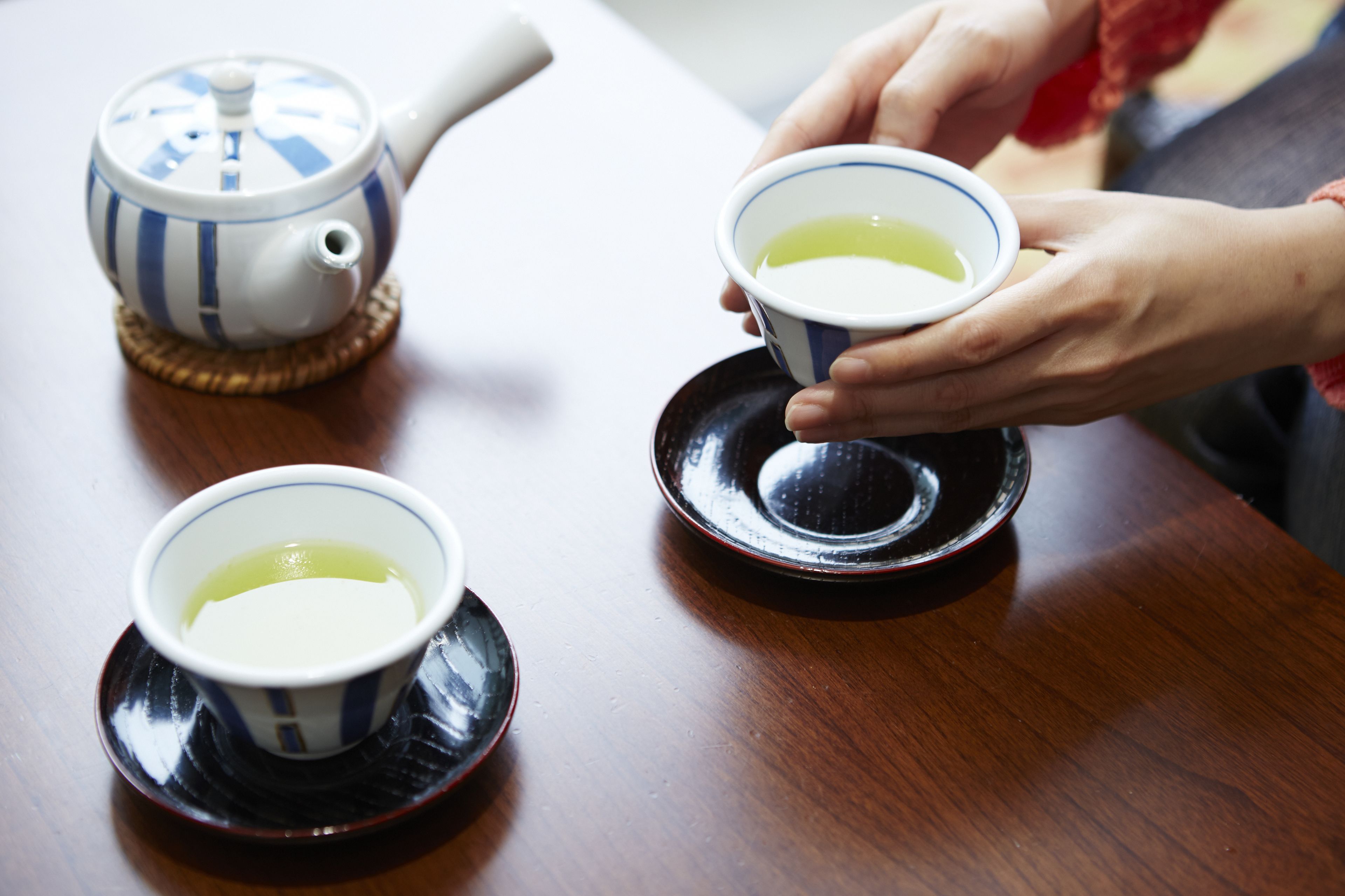 A wooden table with three teapots and cups, one of which is being held by a person.