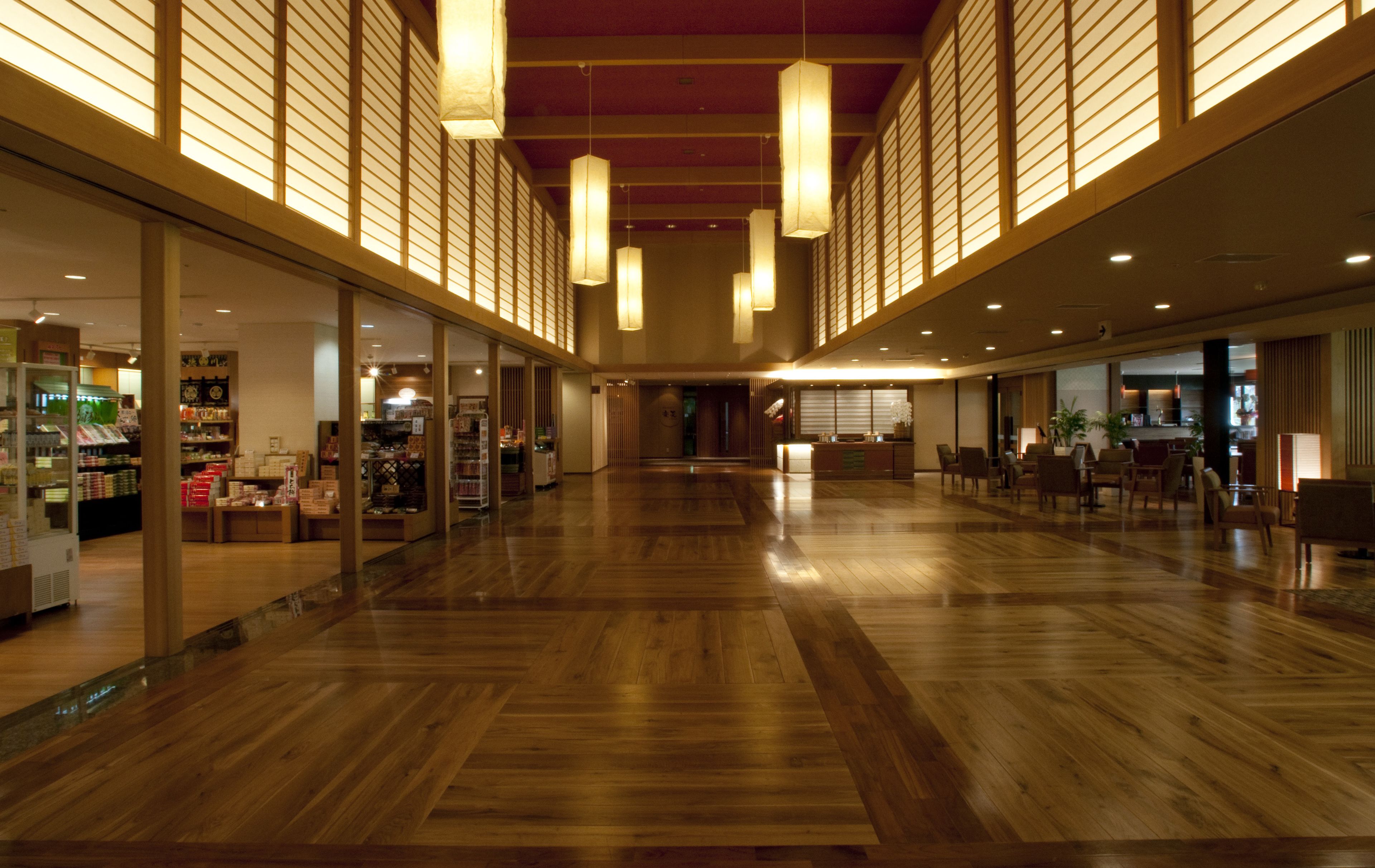 A spacious lobby with wooden flooring, large windows, and hanging lights.