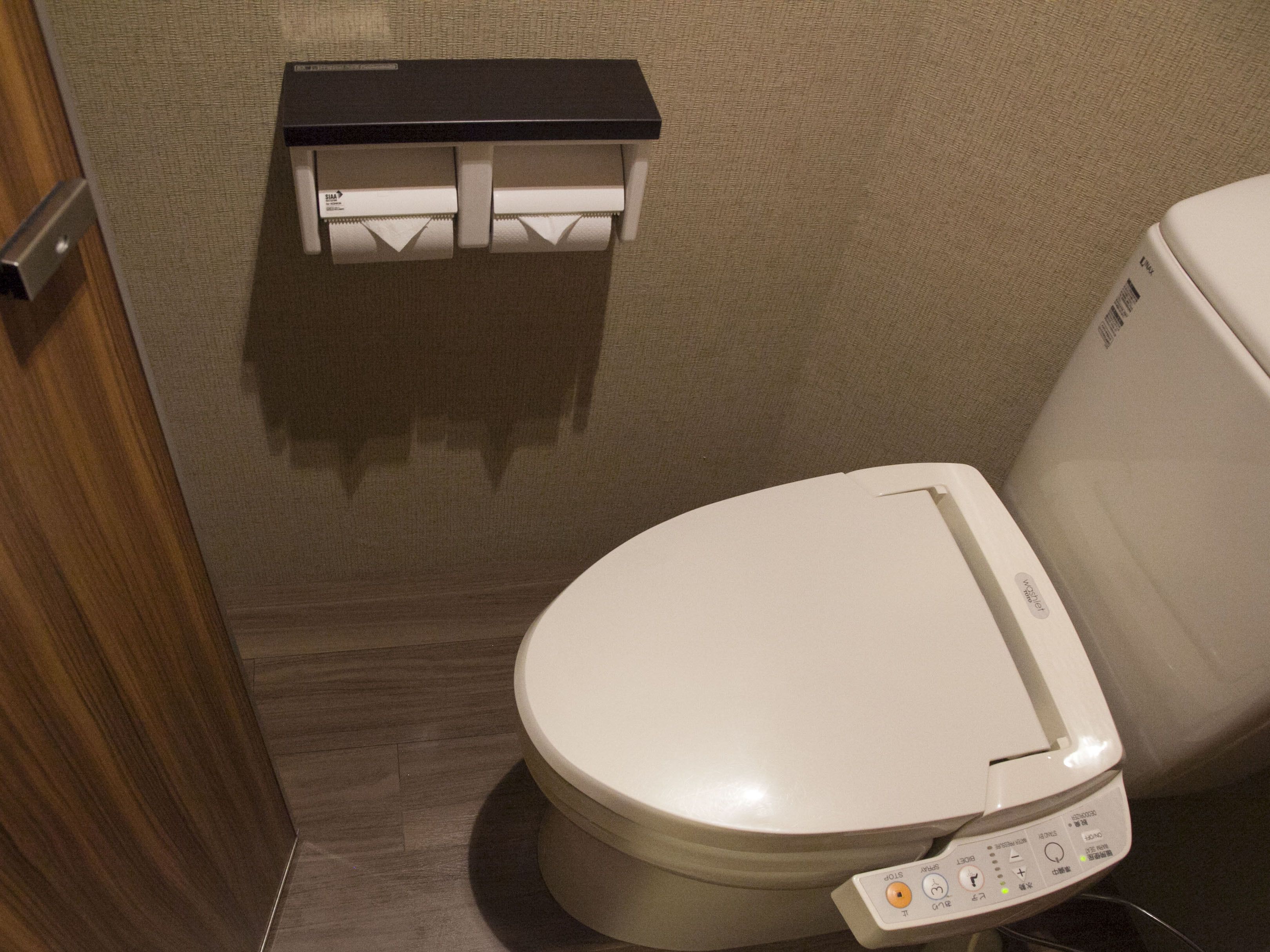 A toilet with a control panel and a toilet paper holder on the wall.
