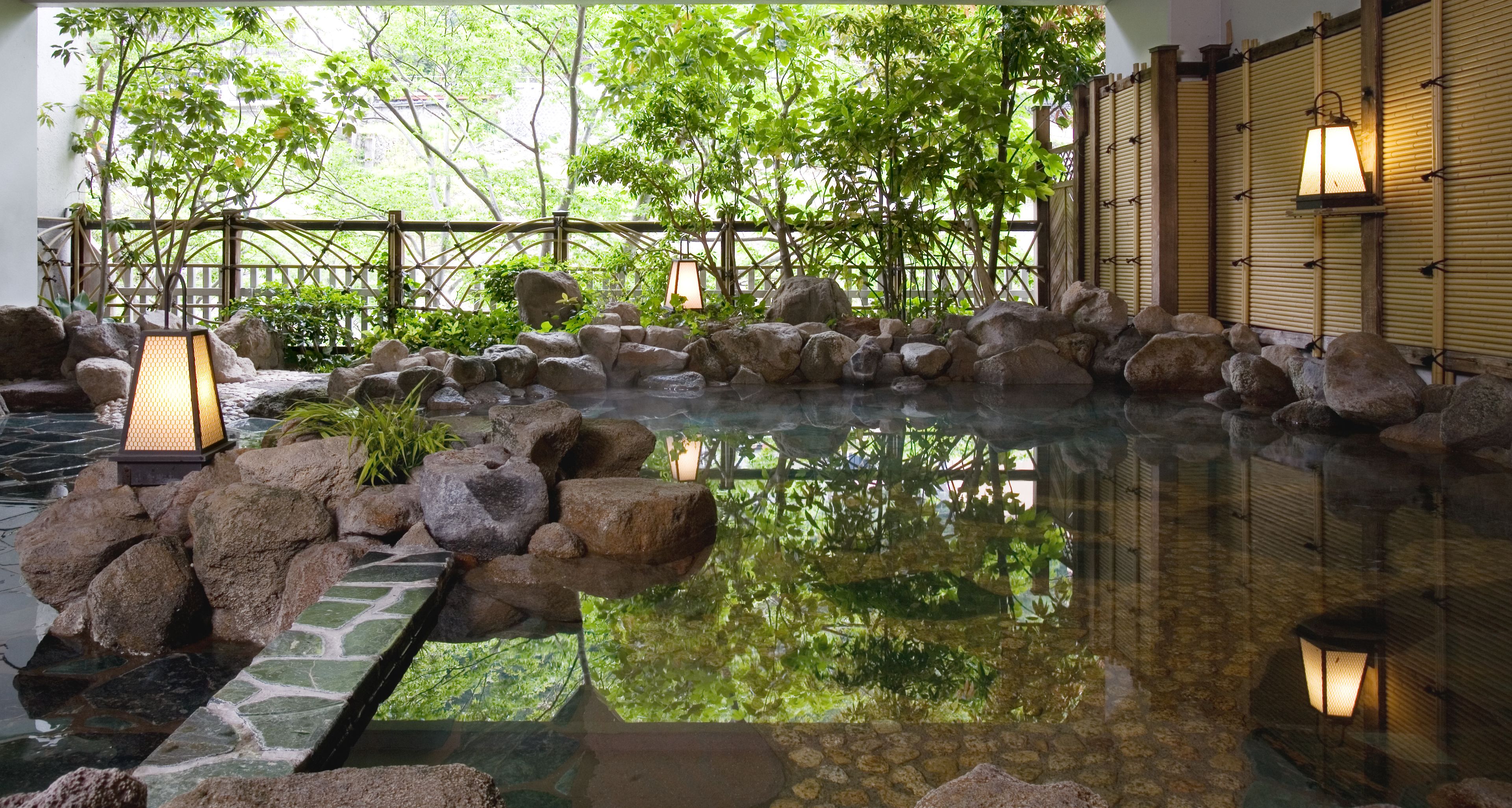 Un jardin intérieur paisible, avec un bassin bordé de rochers, des murs en bambou et des lanternes traditionnelles.