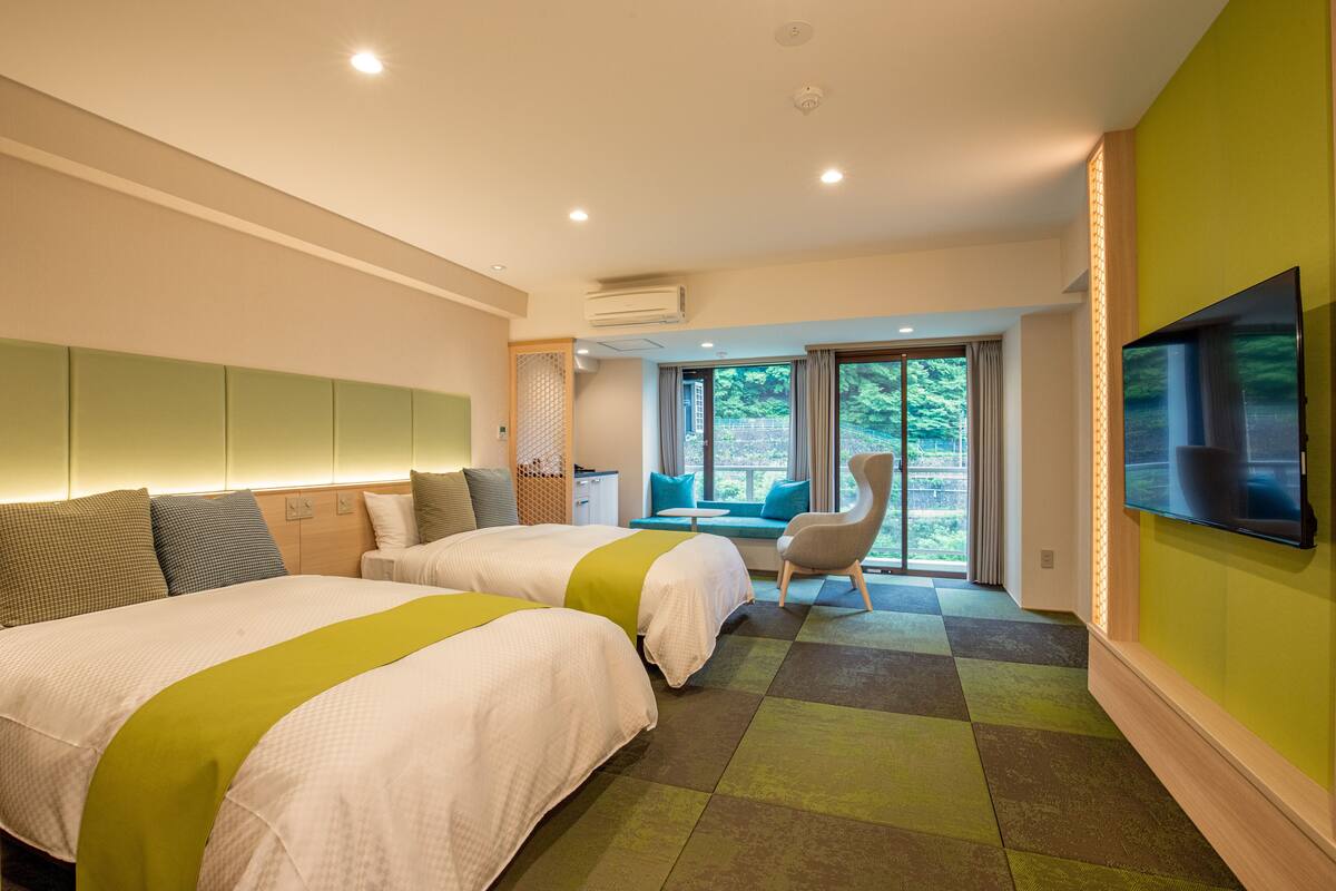 A hotel room with two beds, a TV, a chair, and a view of greenery outside.