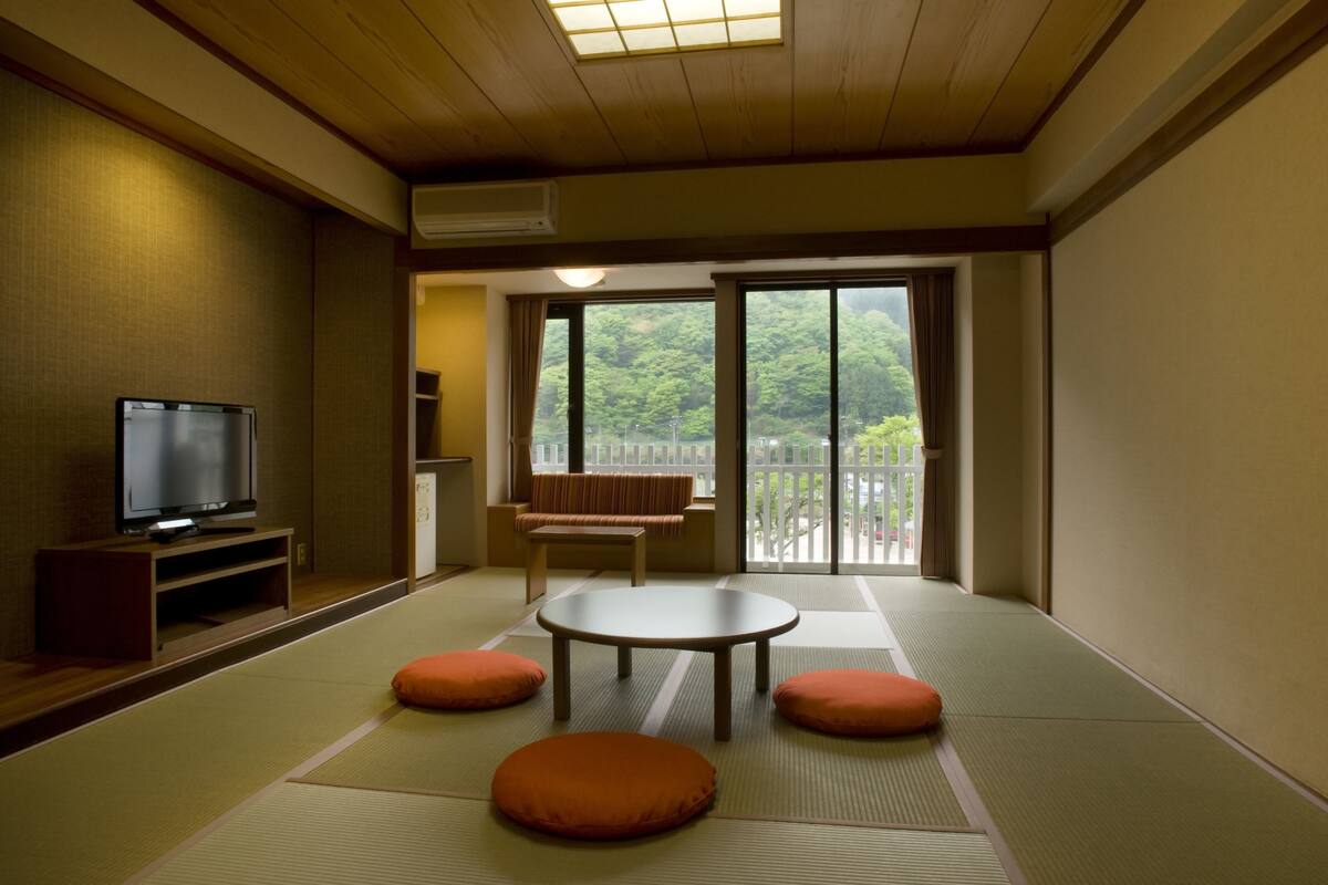 A traditional Japanese room with tatami flooring, a television, a sofa, and a sliding glass door to a balcony.