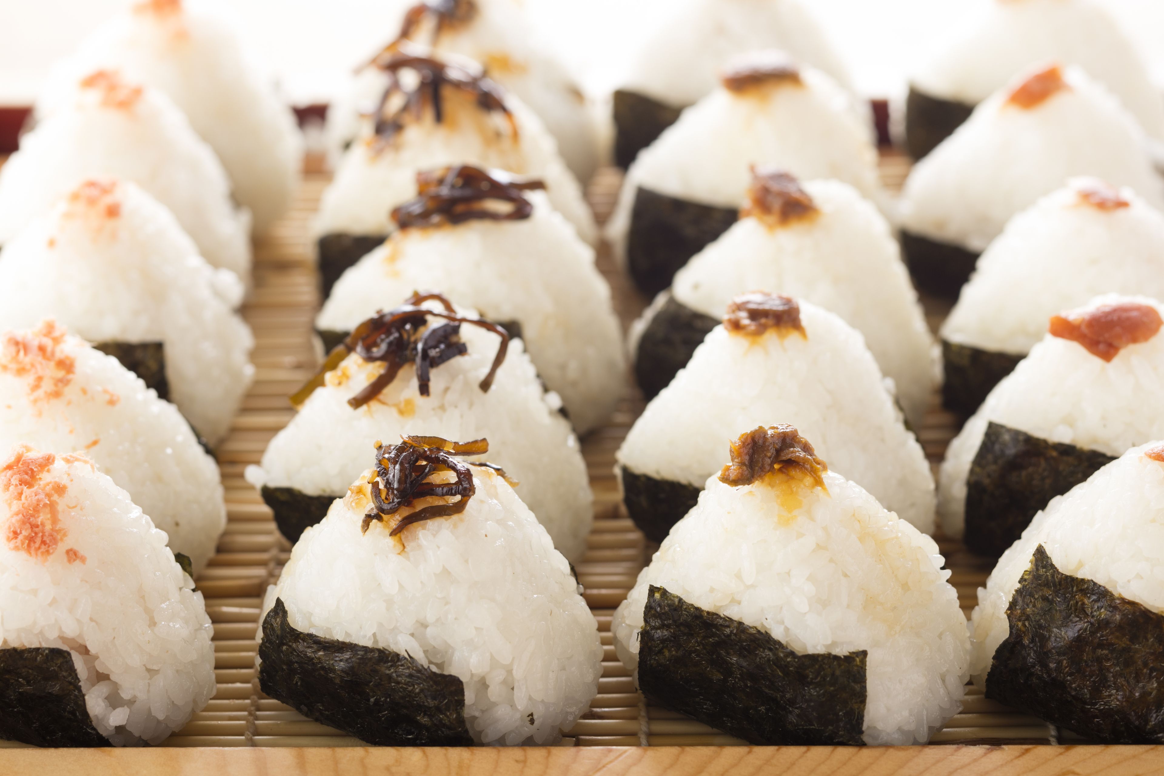 A tray of sushi rolls with rice and seaweed, some topped with sesame seeds and other toppings.