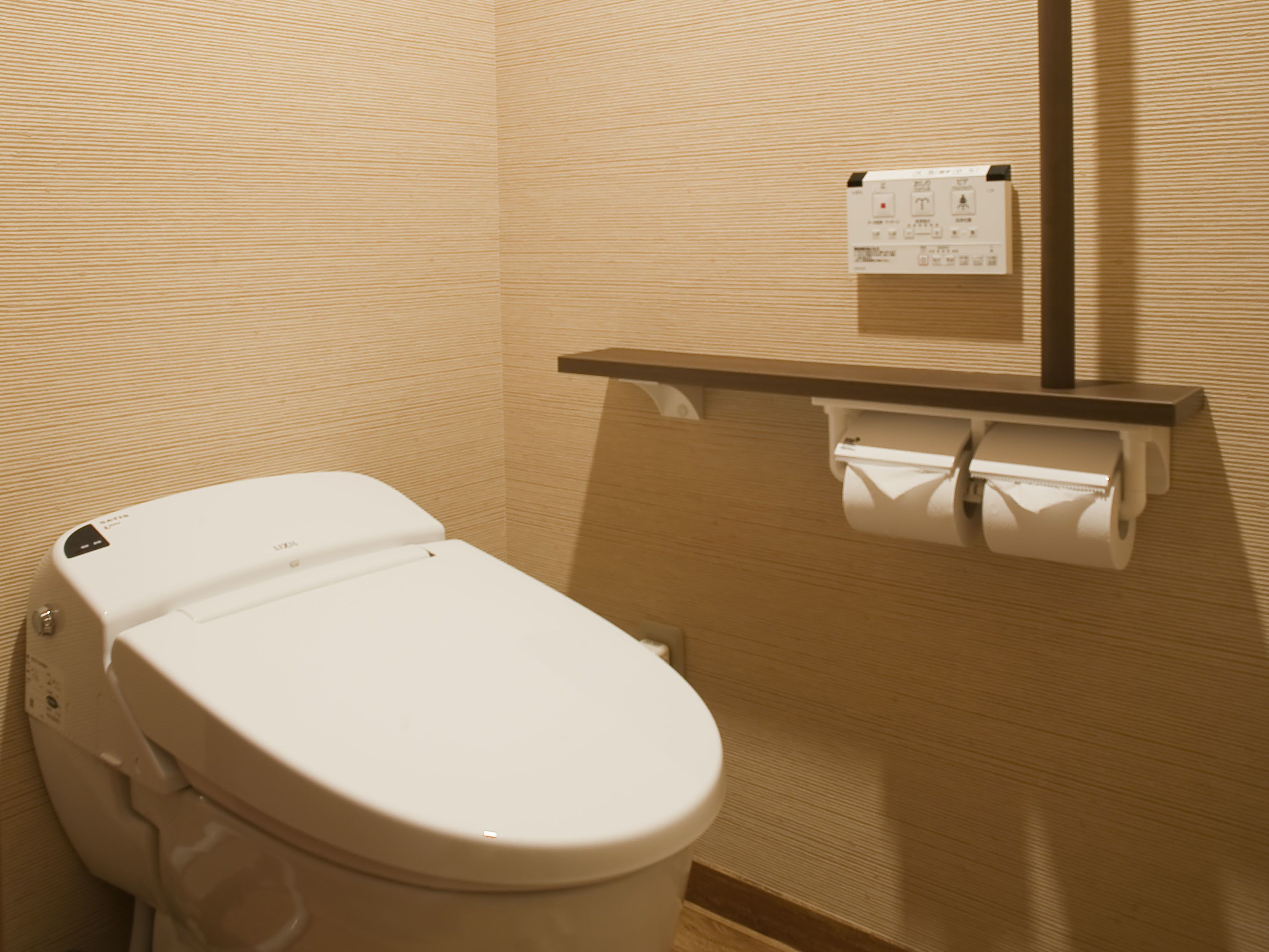 A white toilet with a paper towel dispenser and a hand dryer mounted on the wall.