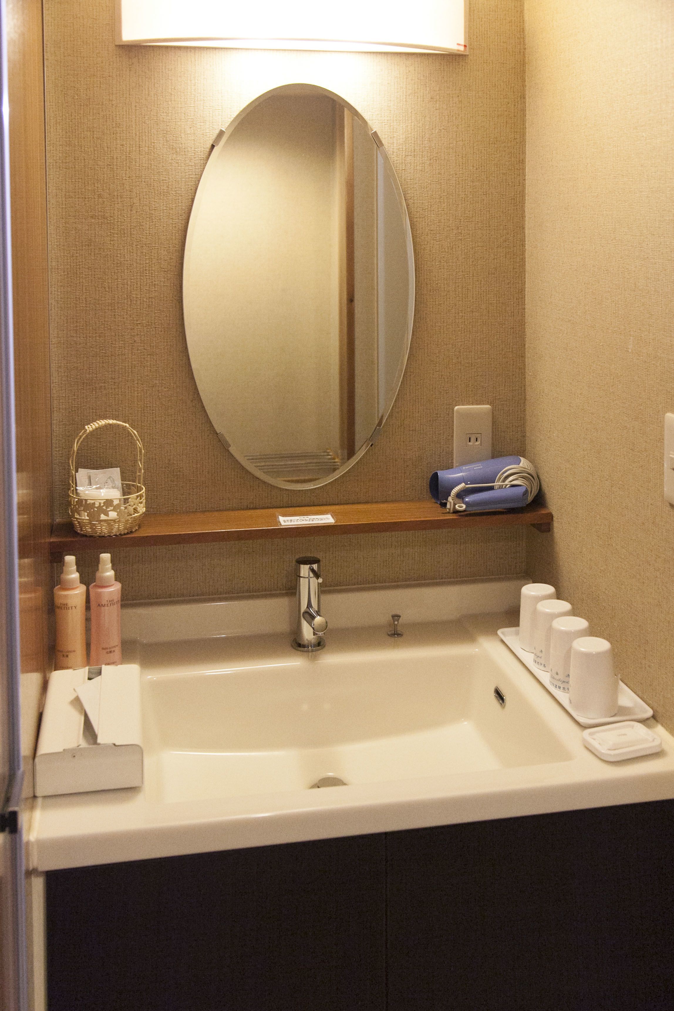 A hotel bathroom with a large mirror, a sink, and a shelf with toiletries.