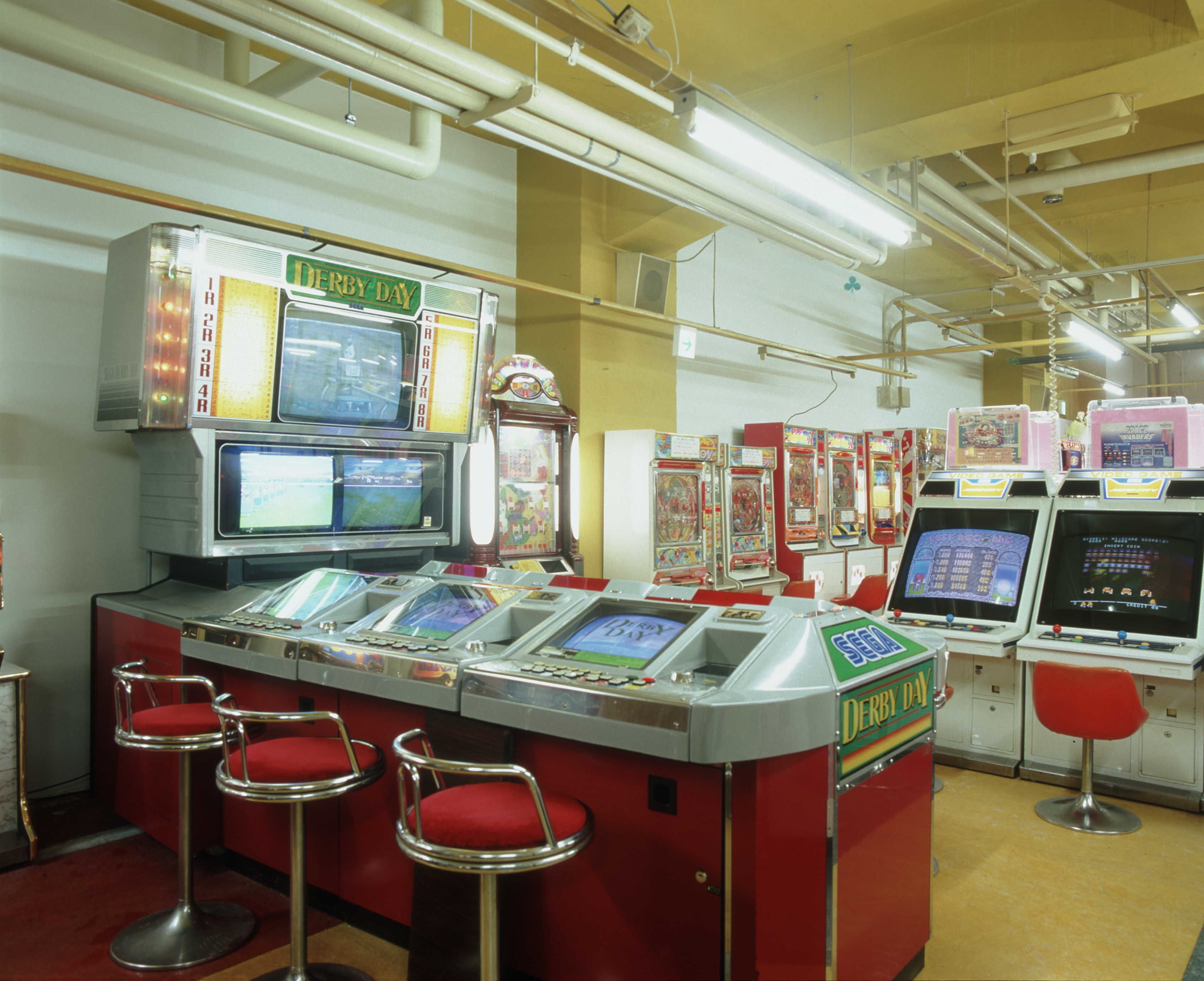 Una hilera de máquinas de arcade con un letrero que dice 'DERBY DAY' y una fila de taburetes rojos delante.