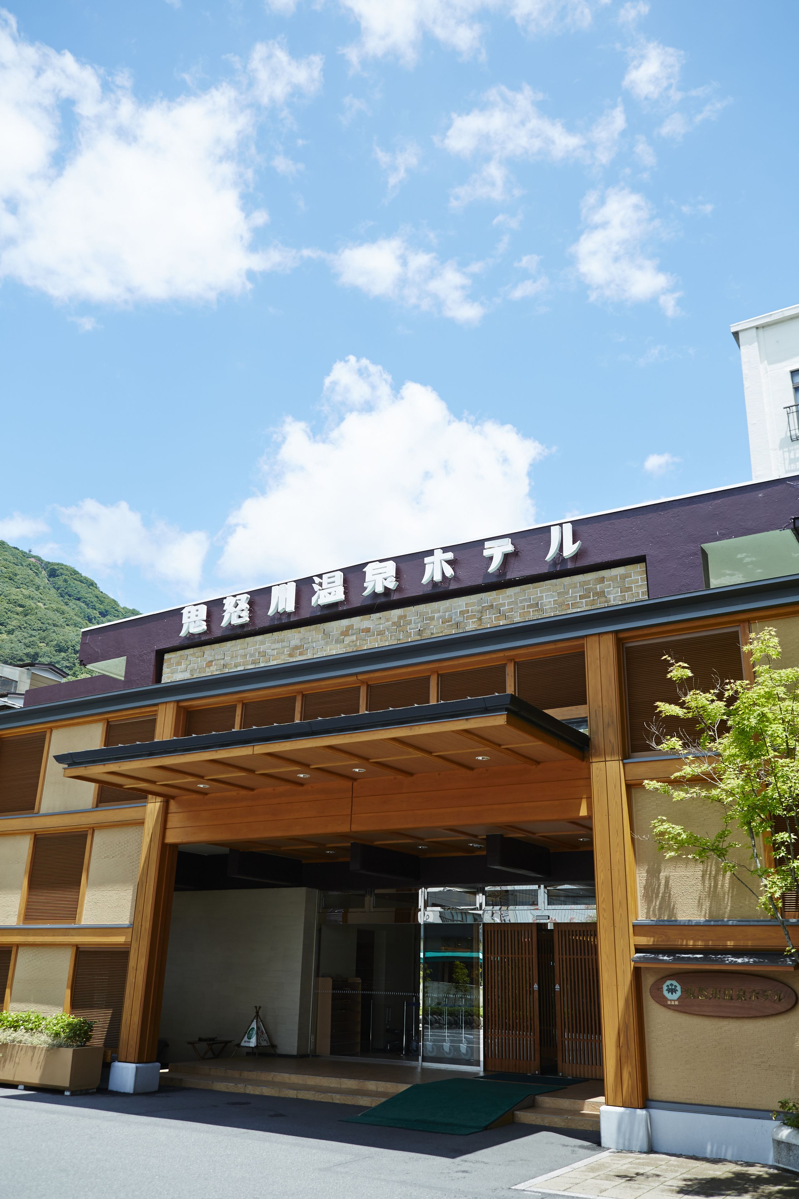 Entrada de hotel con un letrero en japonés, un área de acceso cubierta y vistas al cielo.
