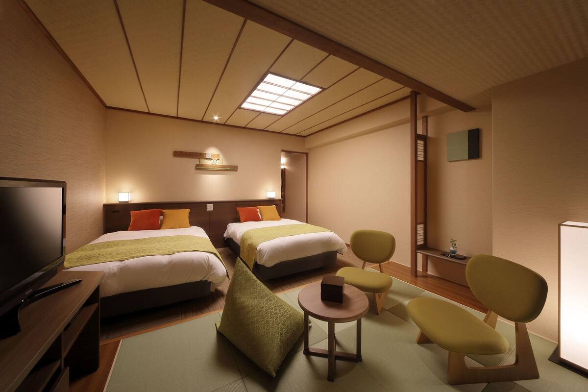 A hotel room with two beds, a television, a small table, and two chairs.